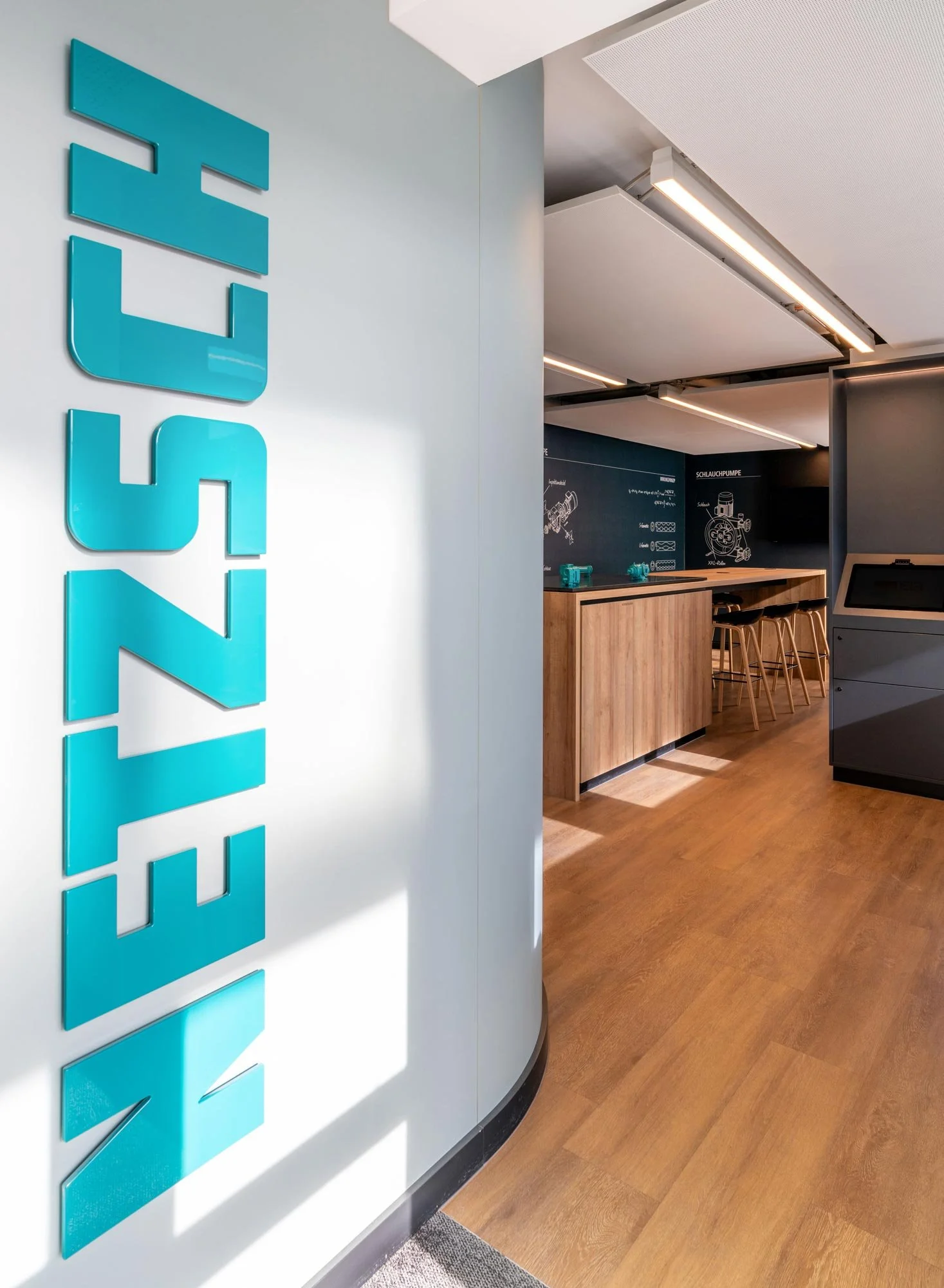 Blaue 3D-Schriftzüge an einer weißen Wand in einem modernen Innenraum, mit einem Holz-Arbeitsbereich und Stühlen im Hintergrund.