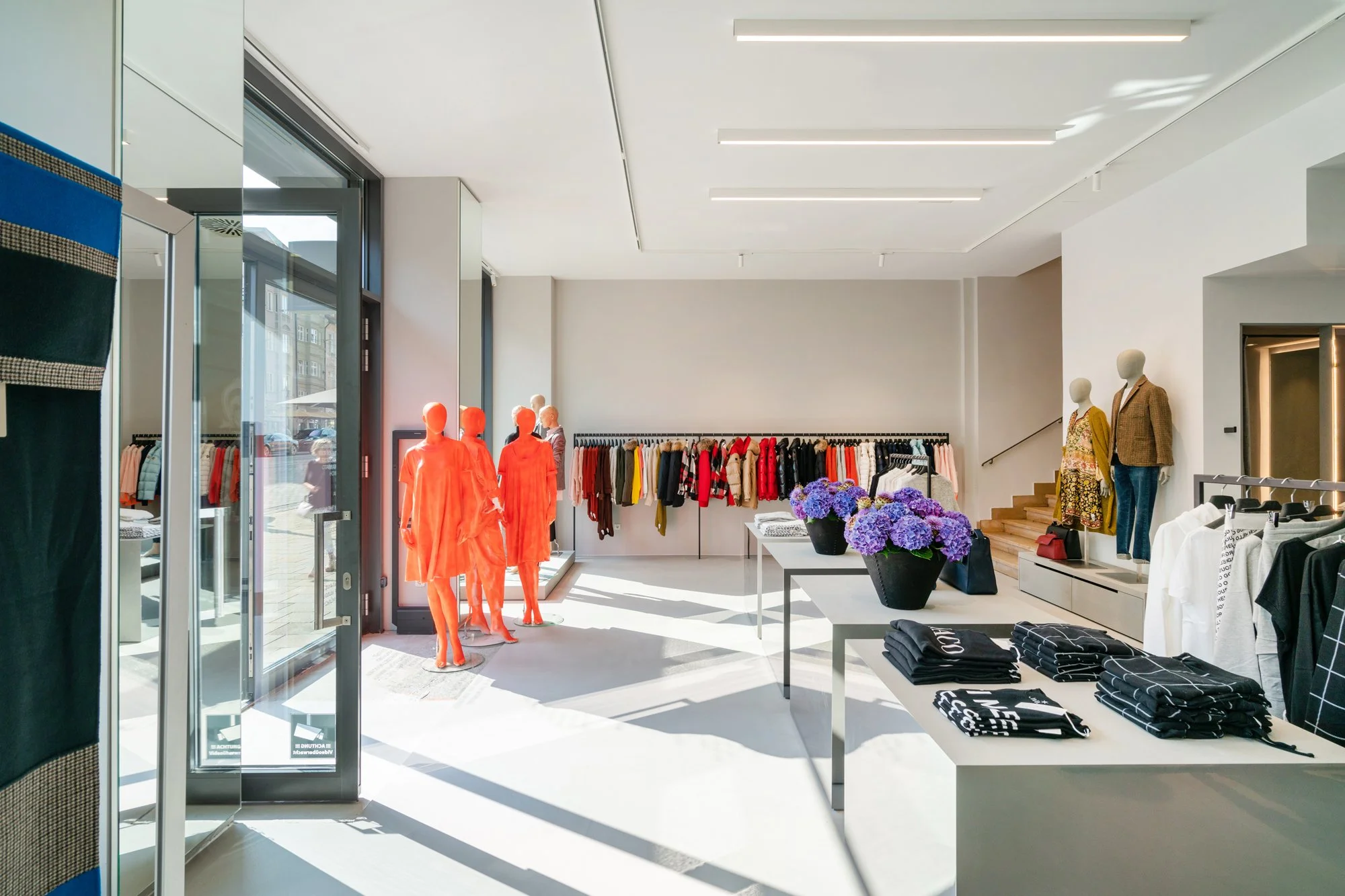 Innenaufnahme eines modern eingerichteten Modegeschäfts mit Kleiderständern, Mannequins und Tischen mit Kleidung, viele Sonnenlichteinfälle