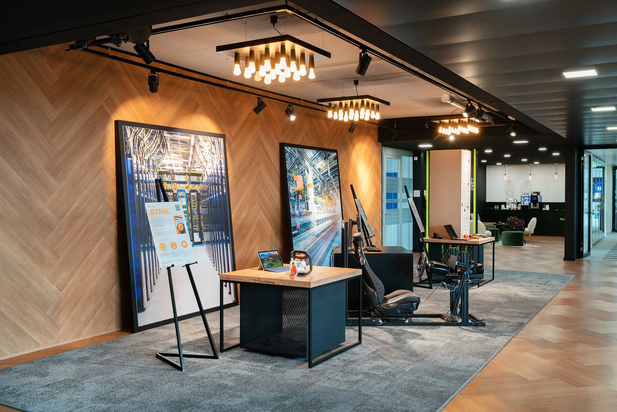 Modernes Büro mit Computerarbeitsplätzen, Wänden aus Holz mit Bildern, dekorative Beleuchtung und gemütliche Sitzecke im Hintergrund.