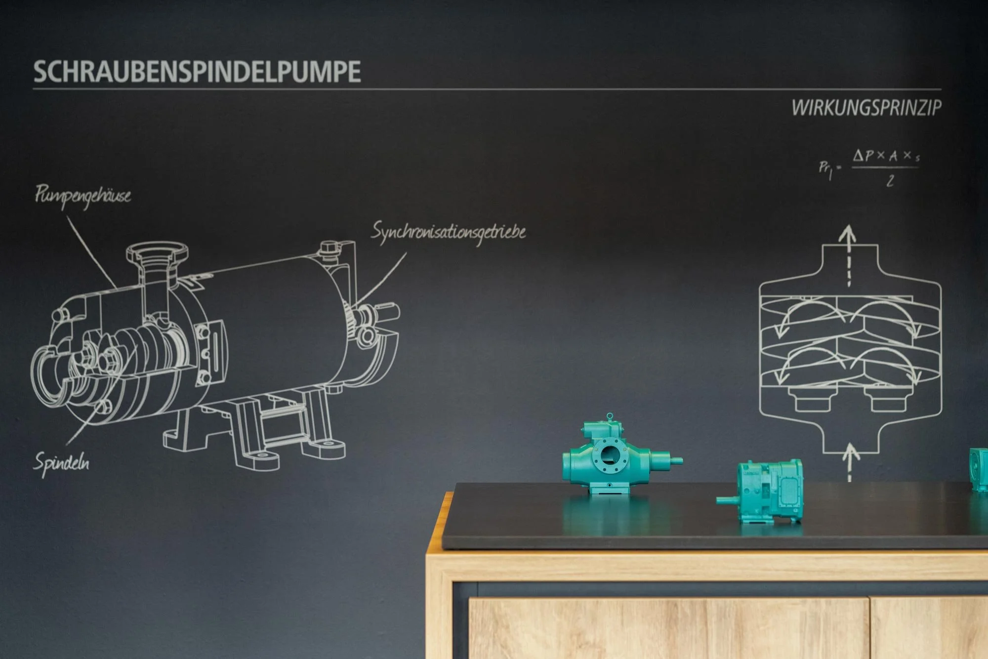 Technische Zeichnung eines Schraubenspindelpumpen, auf einem schwarzen Hintergrund. Vorrätige Pumpenteile in hellblau sind auf einem Tisch im Vordergrund. 