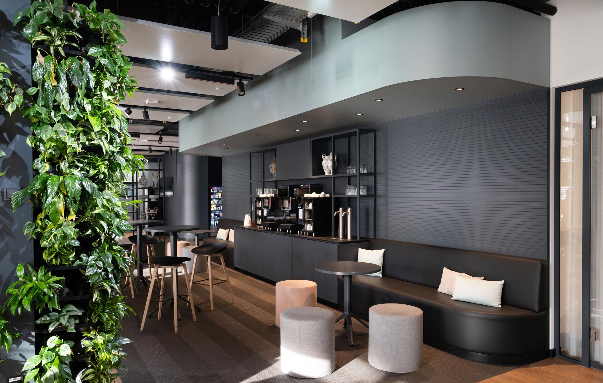 Innenansicht einer modernen, eleganten Café- oder Lounge-Bereich mit schwarzen Möbeln, grünen Pflanzen und Beleuchtung