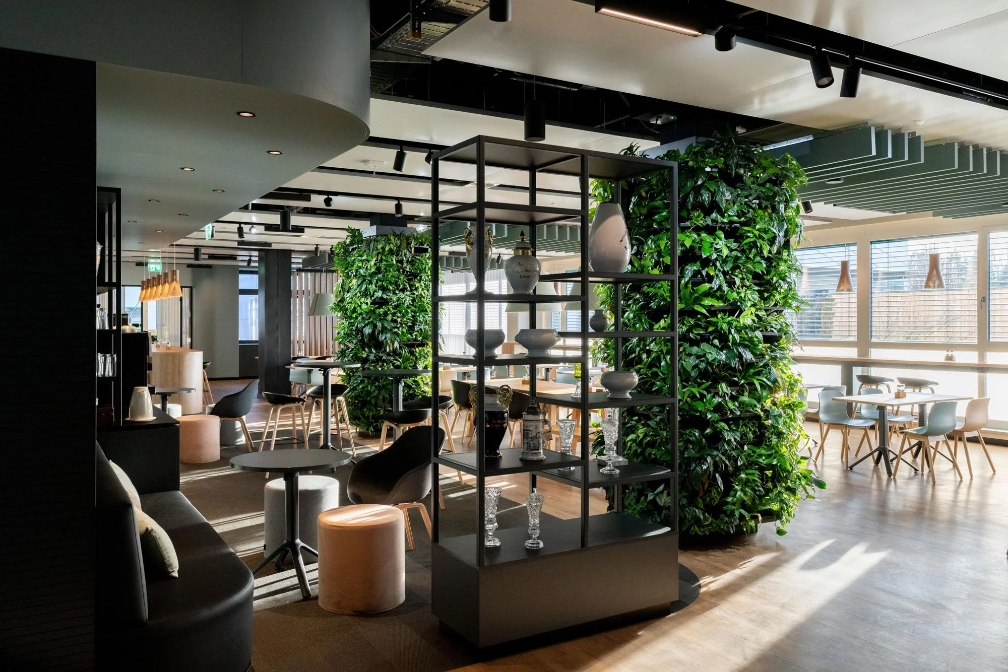Heller moderner Restaurantraum mit großen Fenstern, Grünpflanzen, Sitzgelegenheiten und Dekorationen.