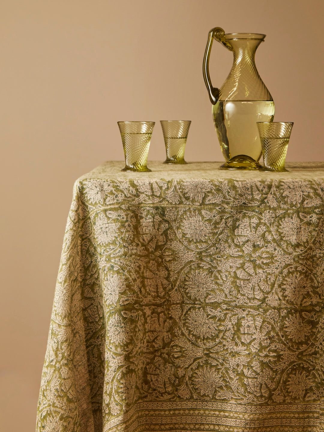 A glass pitcher filled with water and four matching glasses on a table covered with a patterned beige tablecloth.