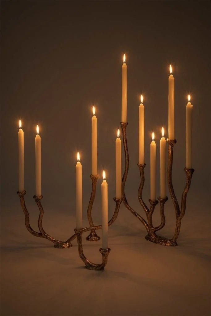 A menorah-shaped candle holder with nine lit candles, designed with a natural, branch-like structure.