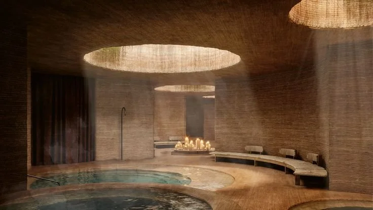 A decorated dining table set for a meal with black dishes, candleholders with lit candles, a bowl of grapes, and a floral centerpiece, in a room with large windows and lush greenery outside.