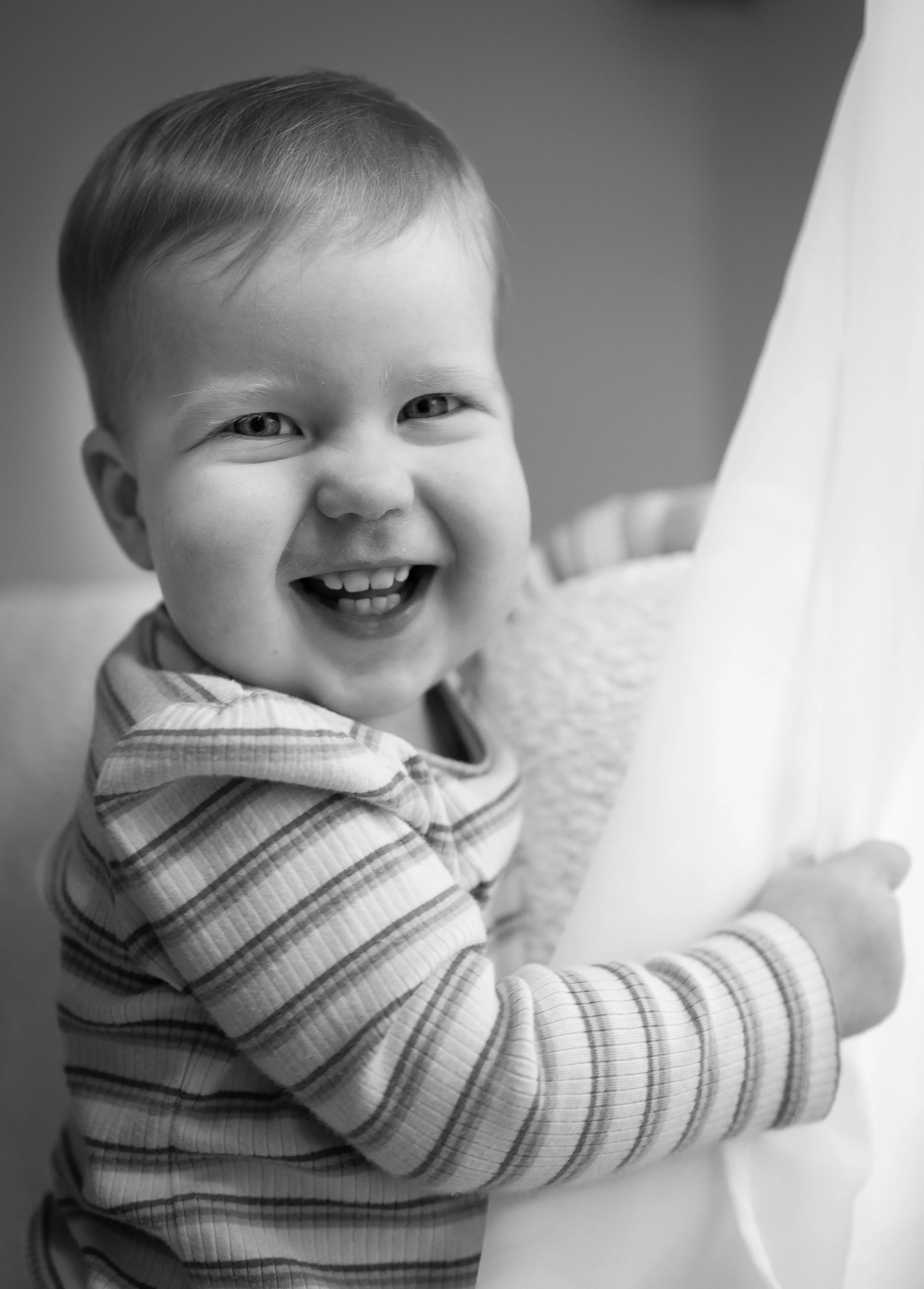 A young boy with a big smile, holding a large white object, wearing a striped long sleeve shirt.