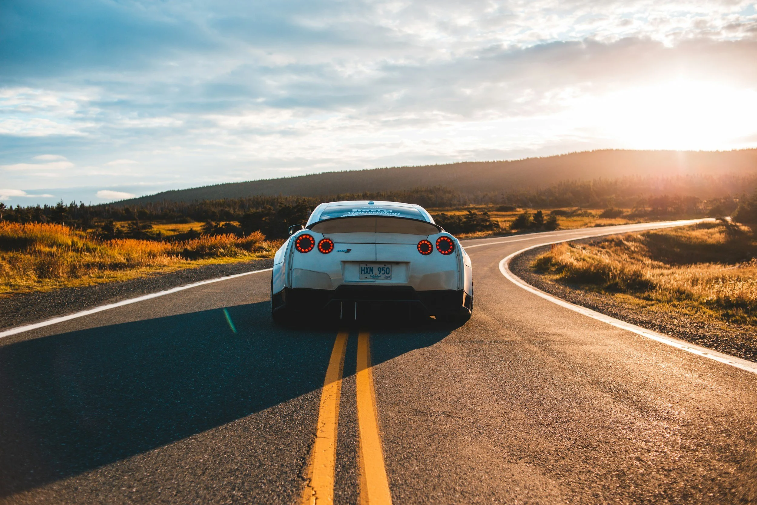 A white sports car driving on a winding road in a rural landscape at sunset.
