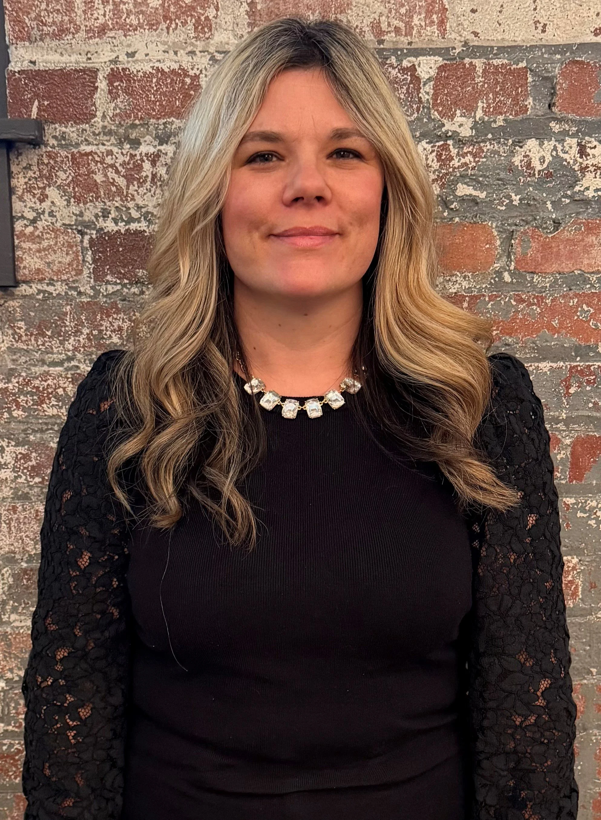 Woman with long hair in a black sweater against a brick background