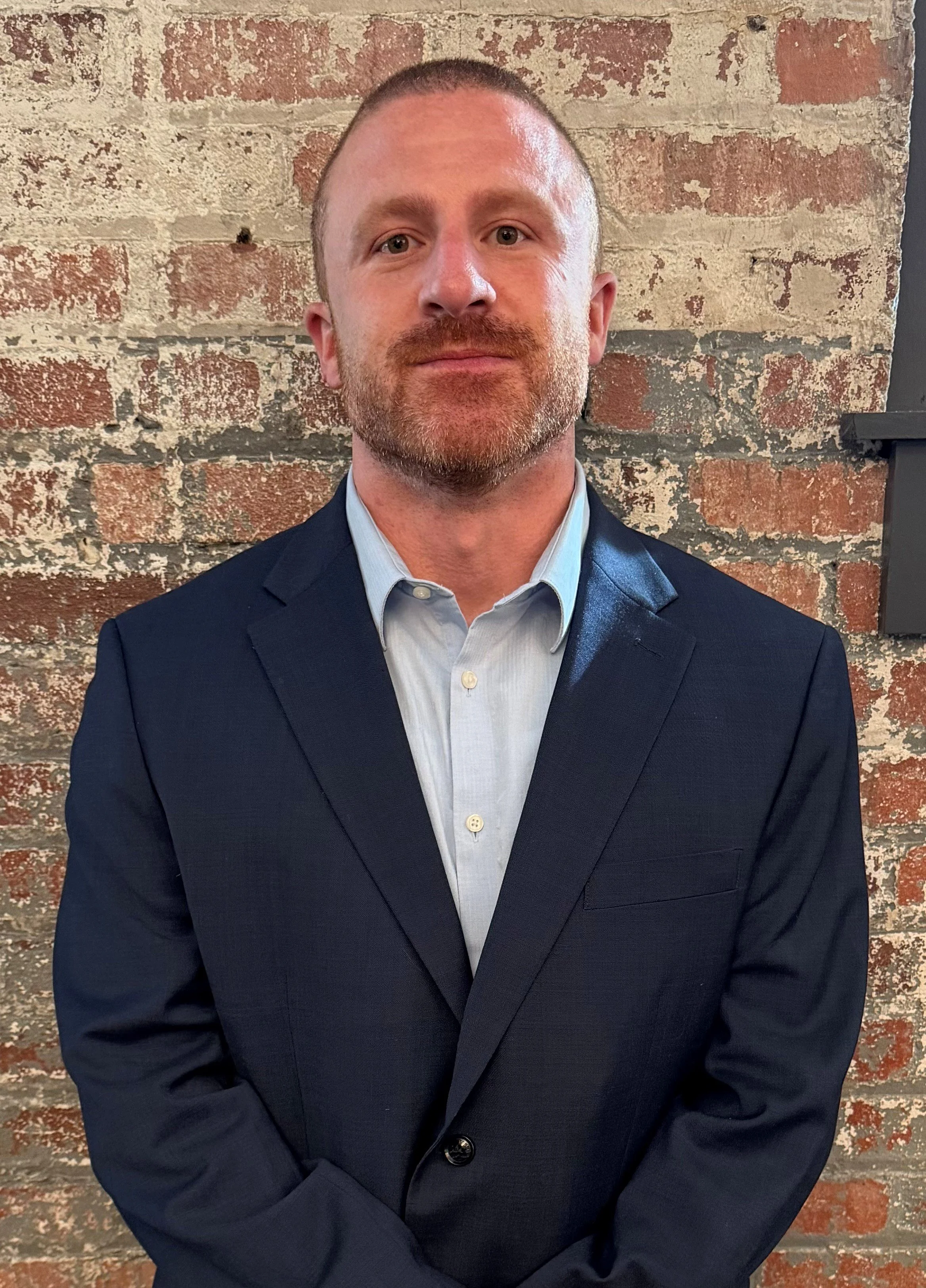 Man in a blue suit jacket against a brick background