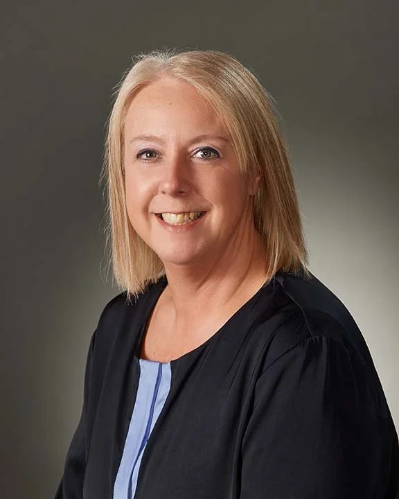 A smiling woman with shoulder-length blonde hair dressed in a black judicial robe over a light blue top