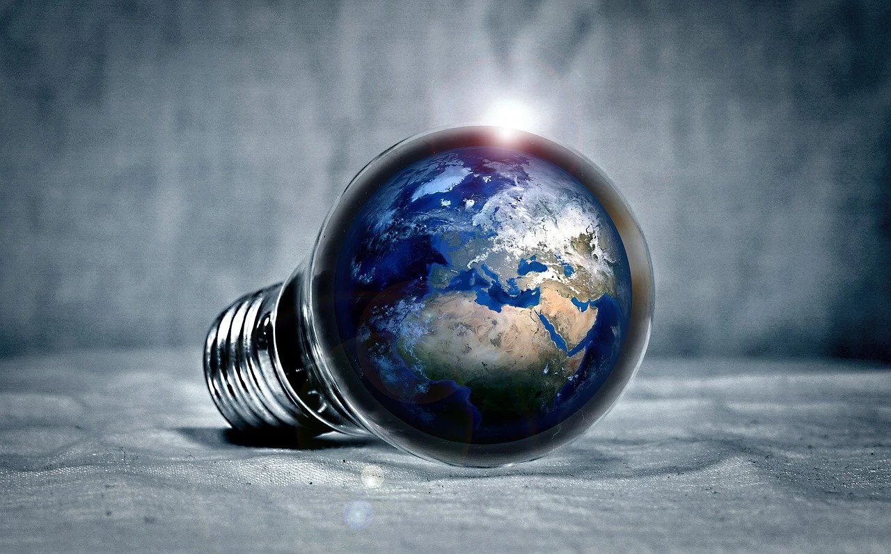 A light bulb with the Earth as the filament, resting on a surface with a gray background.
