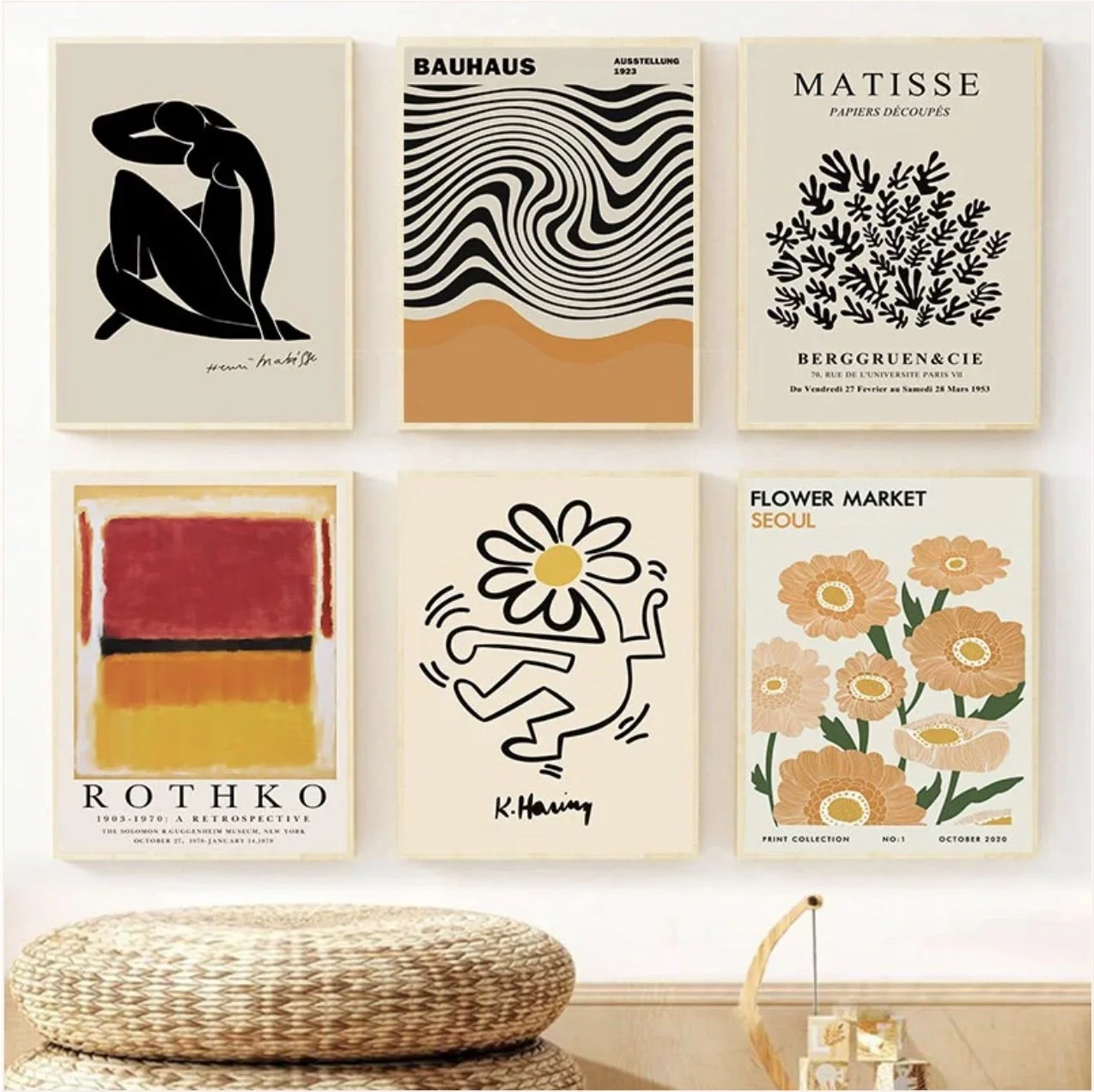 Une collection de six affiches artistiques accrochées au mur, avec des motifs abstraits, floraux et graphiques, dans un style moderne. Moins en bas, un coussin rond en tissu tressé et un petit meuble en bois avec des objets décoratifs.