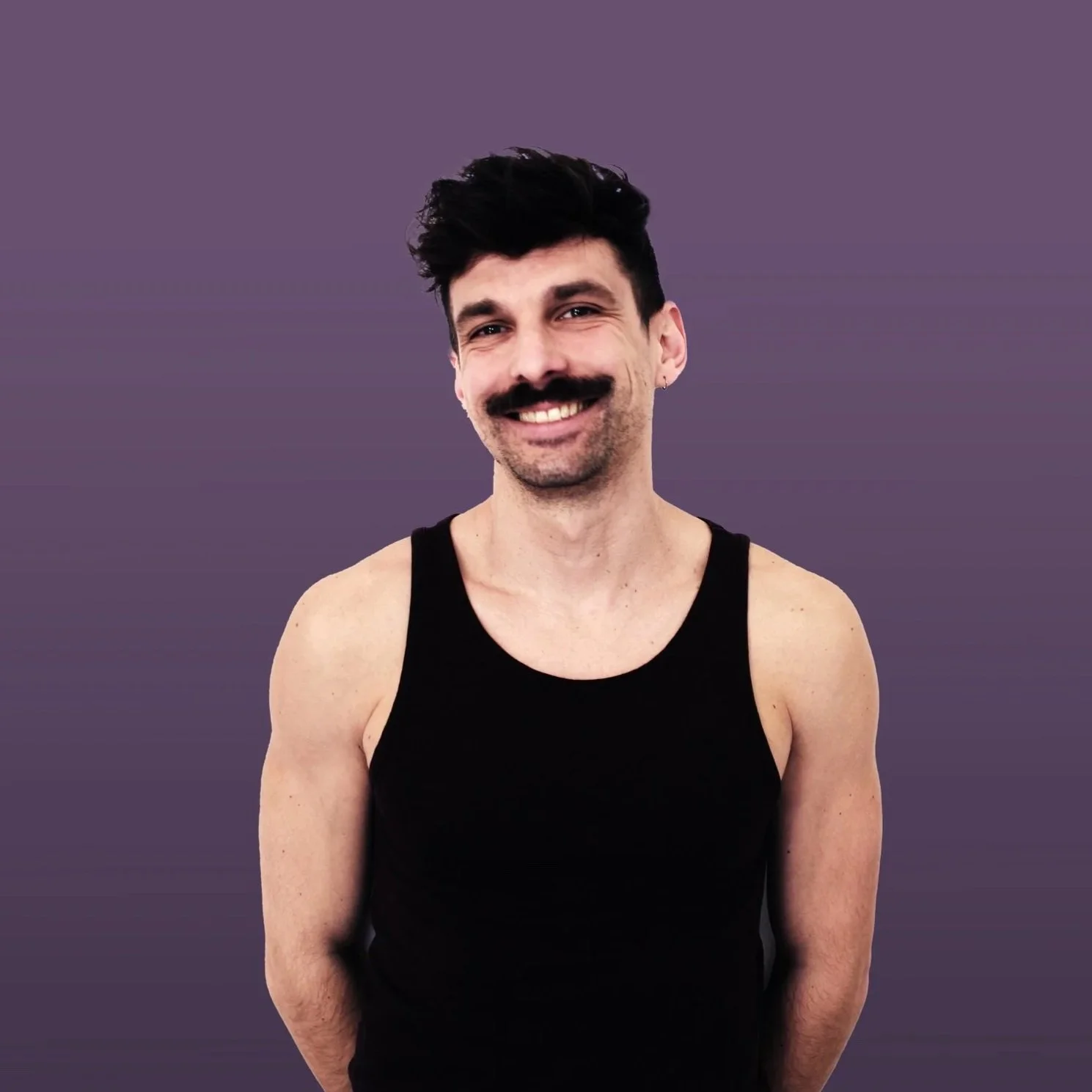 Ein Mann mit dunklem, leicht lockigem Haar, Schnurrbart und Halskette, trägt ein schwarzes Tanktop und steht vor einem lila Hintergrund, lächelnd.