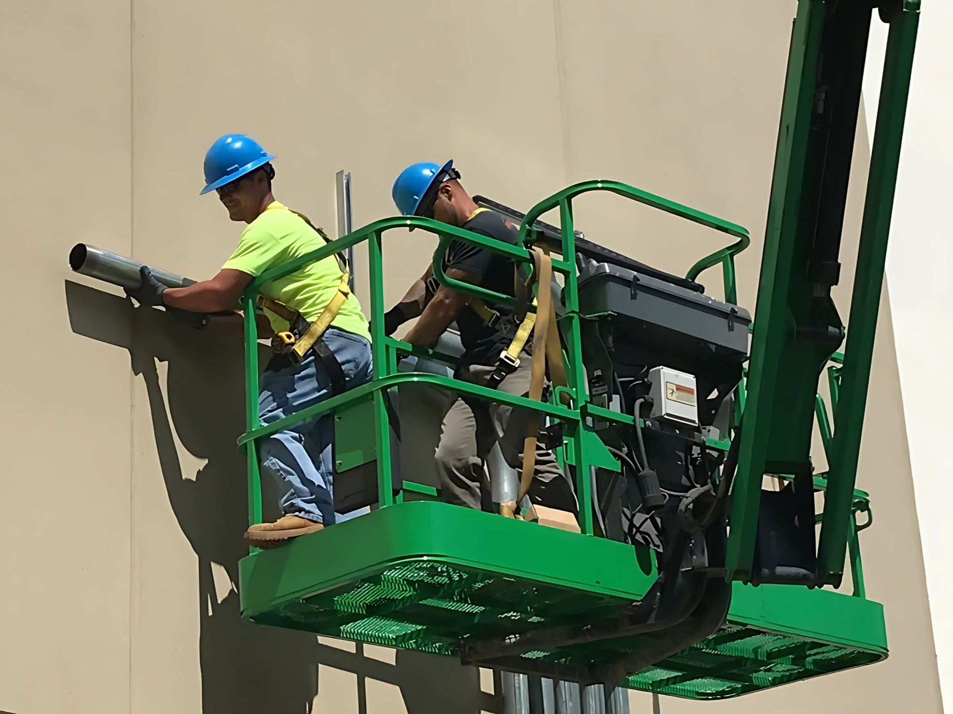 Two workers in helmets operating a lift, working on the exterior wall of a building.