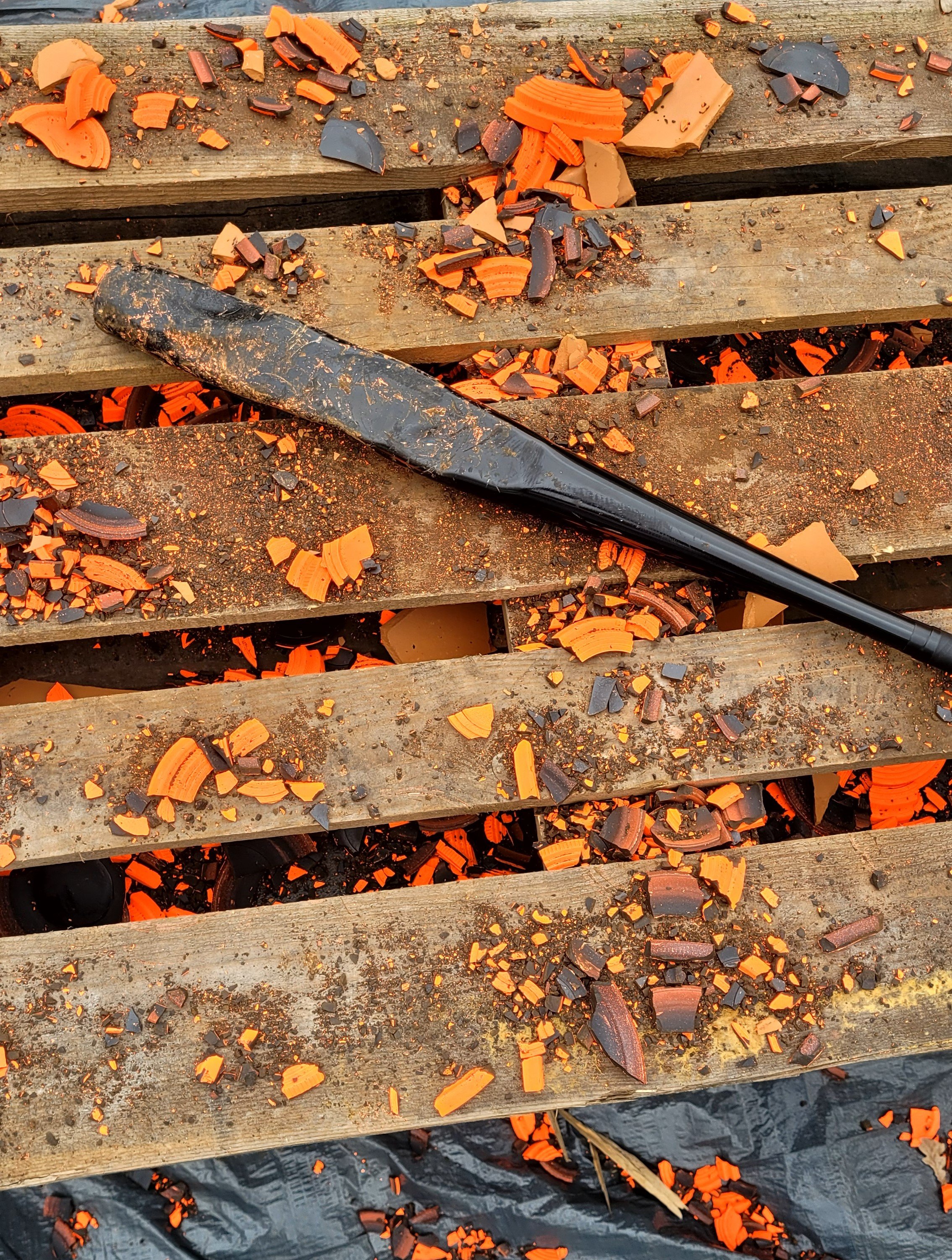 Verbrande en gebroken plasticen klei op houten pallet met een zwarte spatel of schraper ernaast.