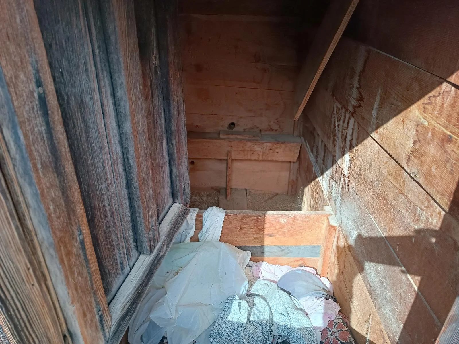 Ahşap duvarlar ve zeminde çöp ve kumaş parçaları bulunan boş oda.