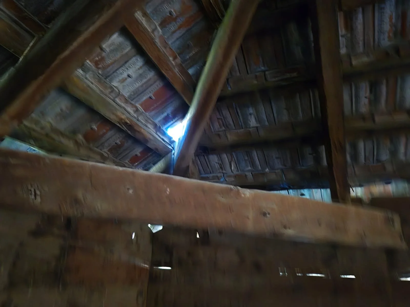 Ahşap bir çatının iç yapısı ve kirişleri görülüyor, çatının hemen üzerinde ışık sızması mevcut.