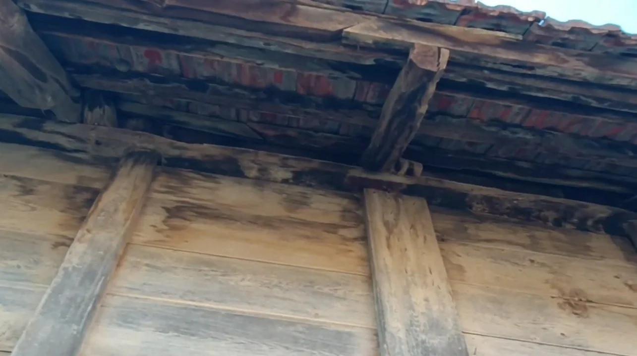 Eski ahşap ve taş yapı with ahşap destekler ve çatlayarak dökülen çatı kaplaması.