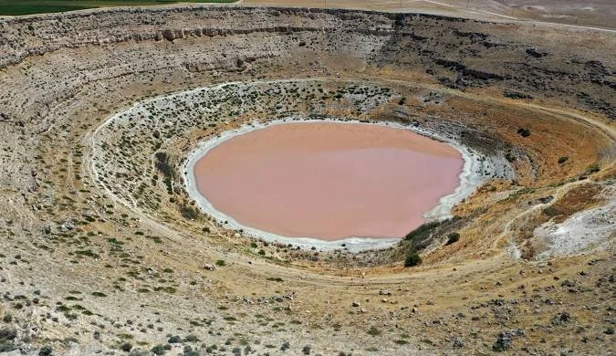 Dağlar ve doğal arazi ortamında, içinde soluk pembe su bulunan göl.