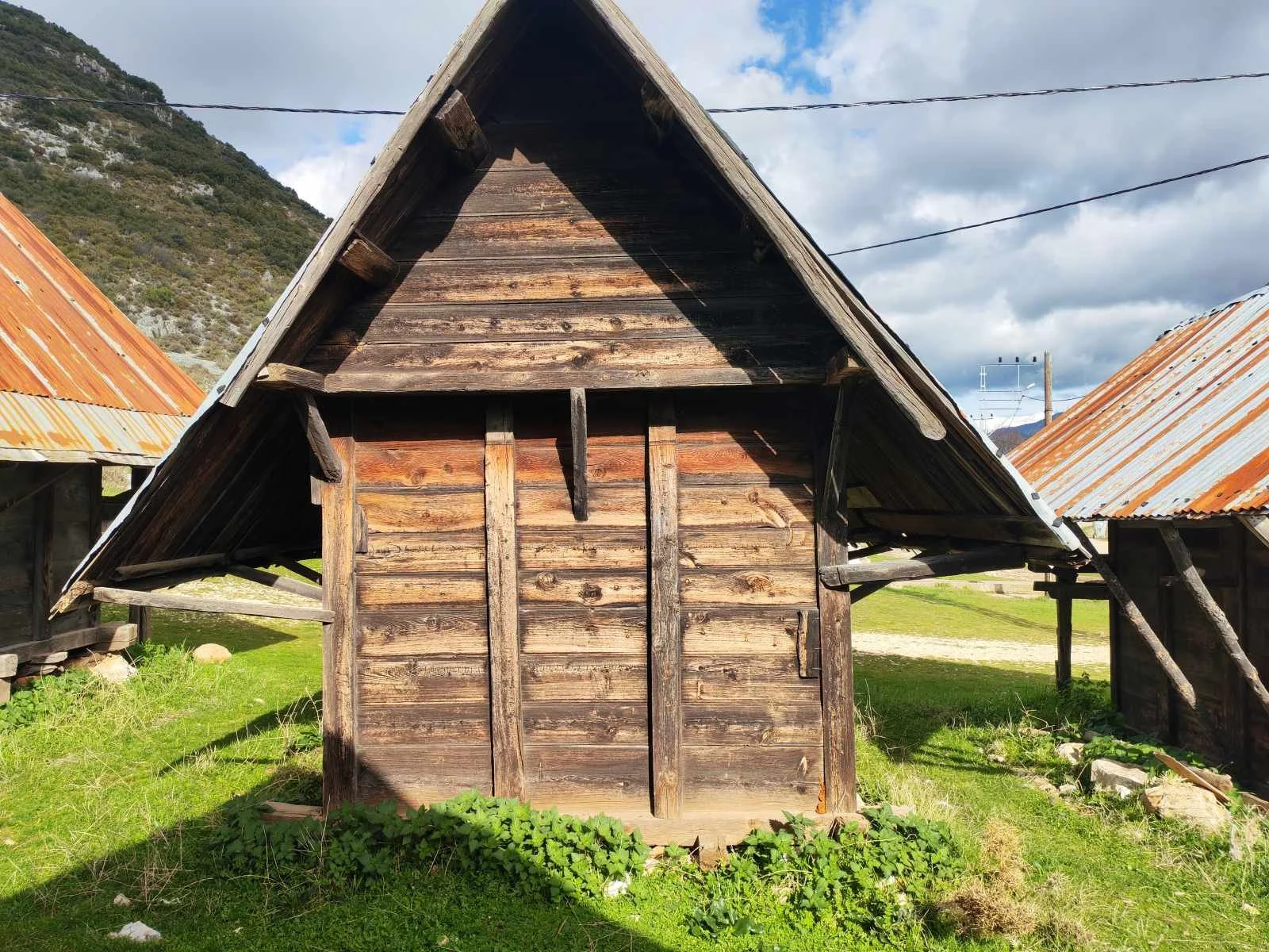 Ahşap bir köy evi ve arka planda dağlar ve mavi gökyüzü.