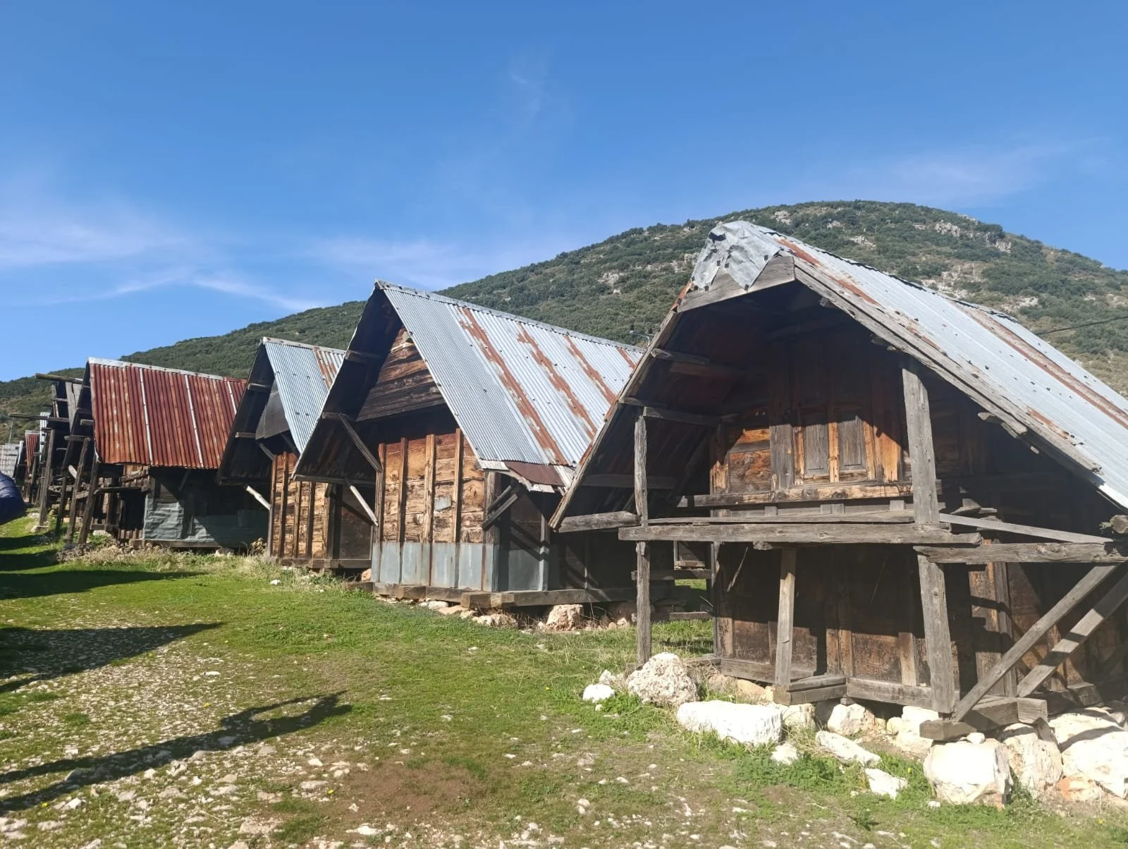 Dağlık alanda sıralanmış, ahşap ve metal çatılı eski küçücük kulübeler.