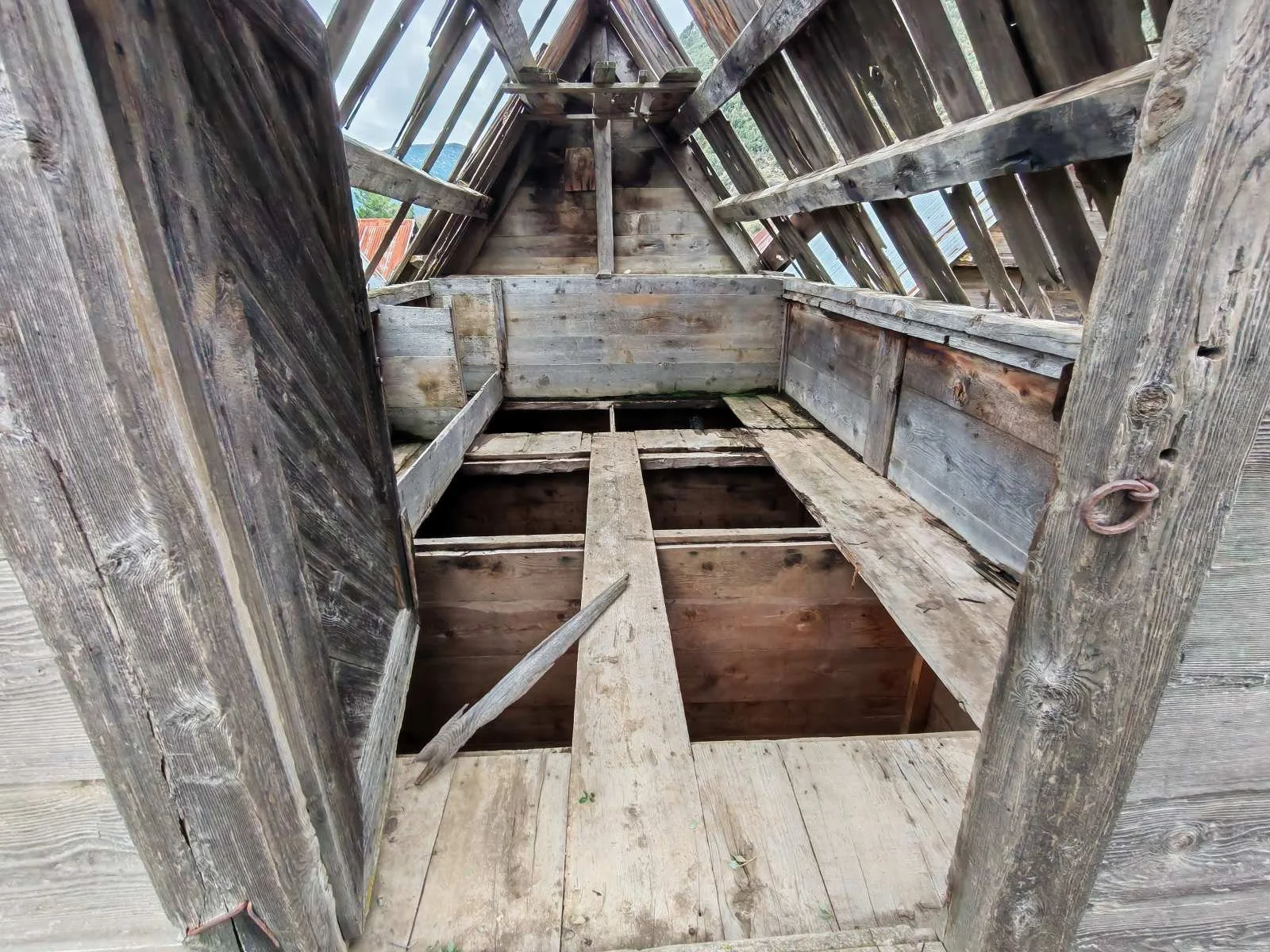 Duvardan görülen, ahşap bir evin çatısının iç kısmı, bazı tahtalar eksik veya kırık, eski ve kullanılır durumda.