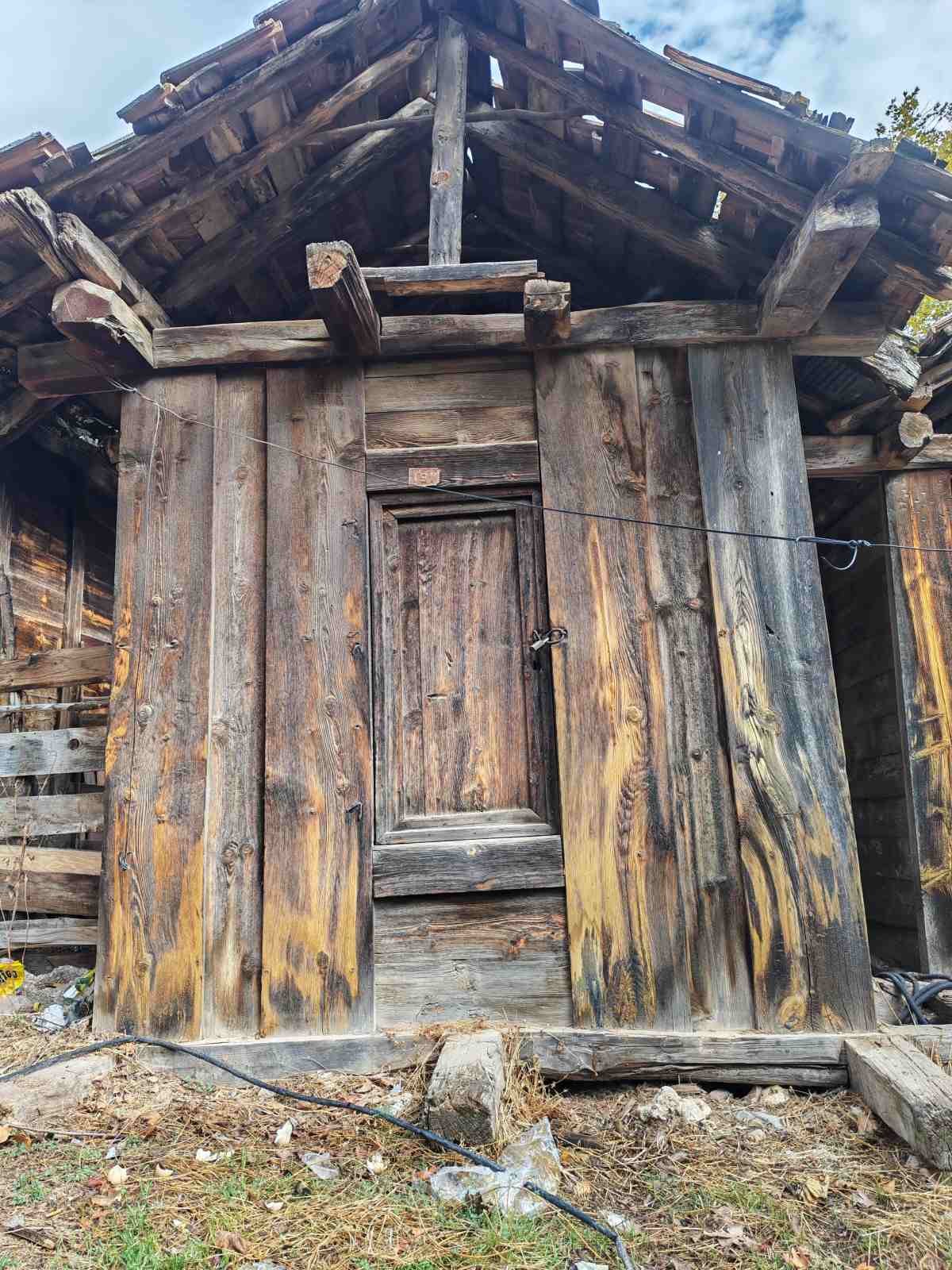 Ahşap eski ve bakımsız bir kulübe. Kapısı kapalı ve etrafında dağınık malzemeler var.