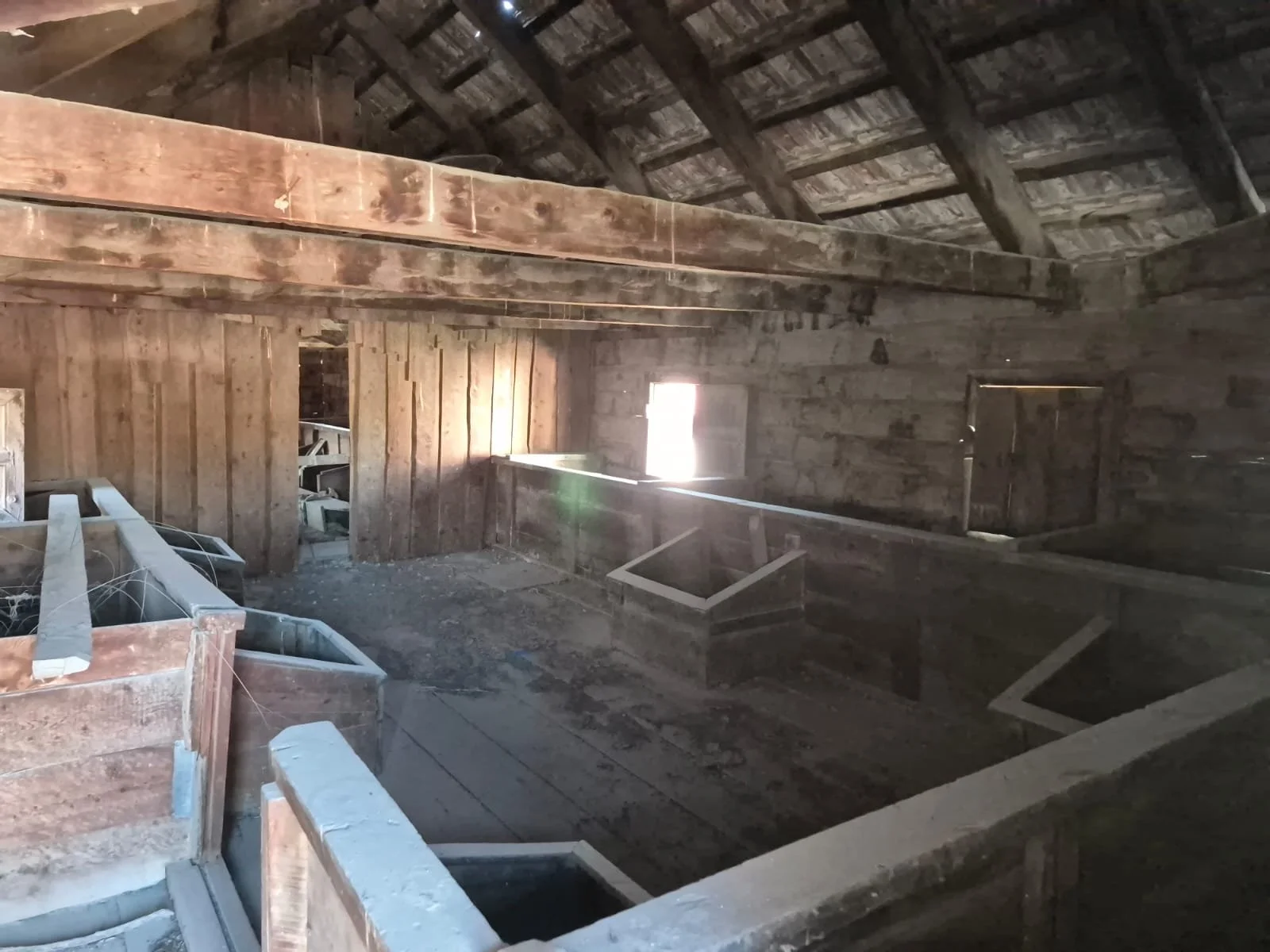 Eski, ahşap ve taş malzemelerle yapılandırılmış ahşap bir çatı altında, odanın içi gösteriliyor. Oda boştur ve bazı yapı elemanları görünür halde.