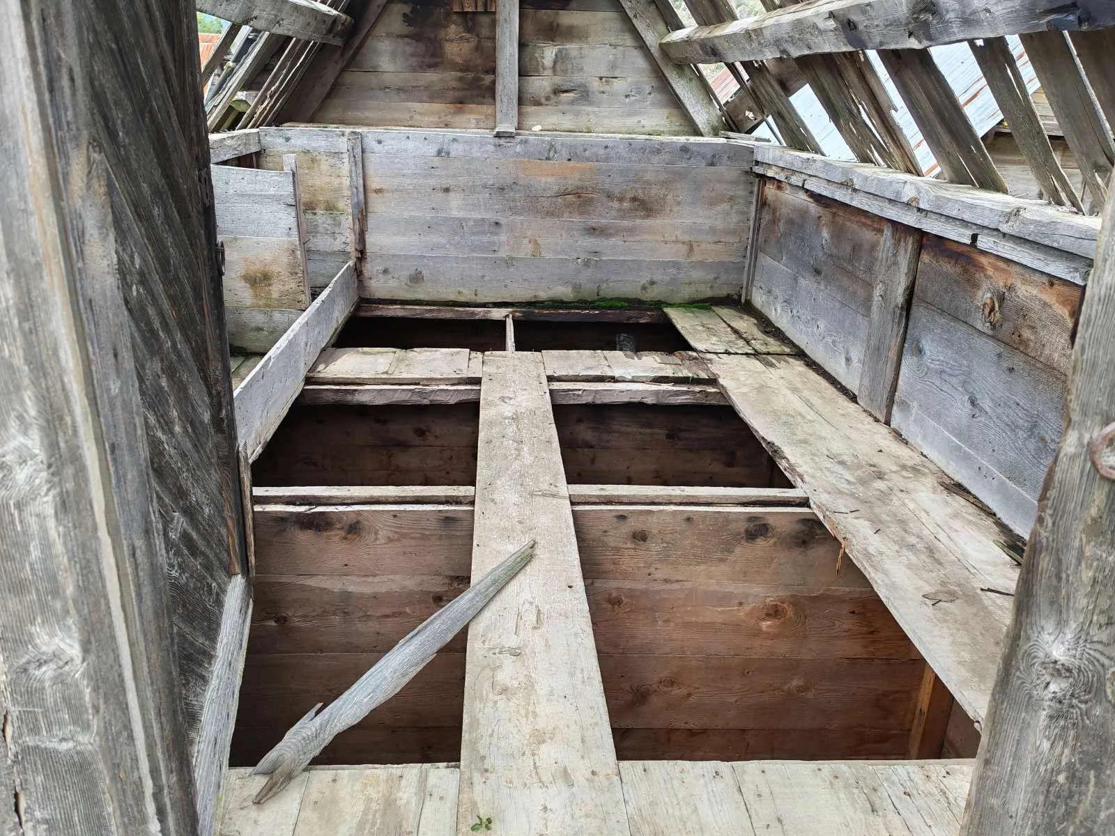 Ahşap yapı ve çatısında hasar bulunan boş bir alan.