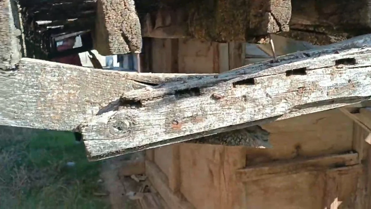 Yaşlı ve hasarlı ahşap direk, arka planda odun ve inşaat malzemeleri.