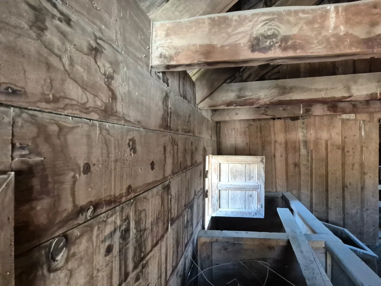 Ahşap tavan ve duvarlar, açık pencere ve merdivenle yapı iç mekanı.