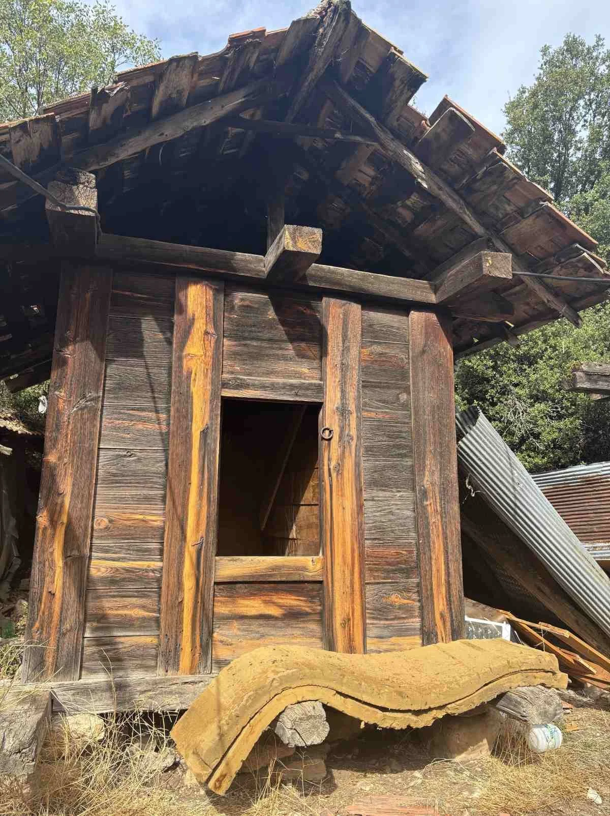 Ahşap ve metal malzemelerle yapılmış, eski ve yıkılmak üzere olan bir ahır veya baraka. Çatı kısımları hasar görmüş ve bazı parçalar devrilmiş durumda. Çevresinde kuru ot ve eski atıklar bulunuyor.