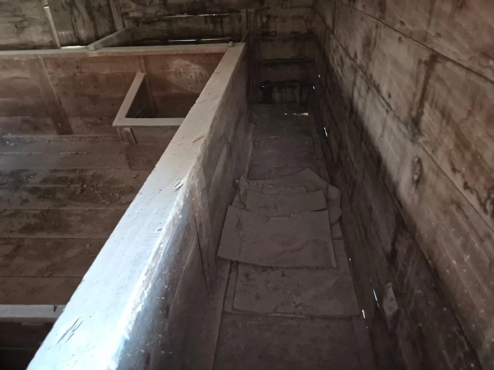 Eski ve ahşap malzemelerle inşa edilmiş, karanlık ve tozlu bir oda veya alan, yerde taşlar var.