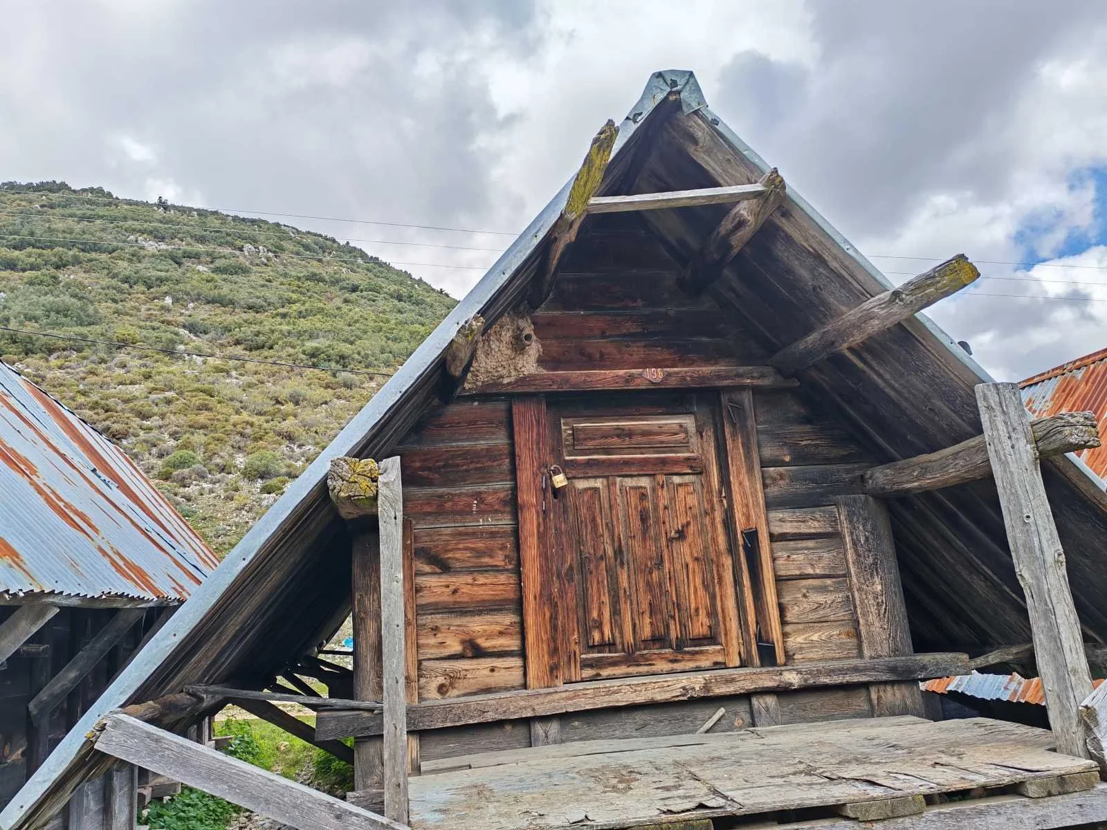 Ahşap ve metal çatıyla eski, küçük bir kulübe. Gün batımı veya hafif yağmur sonrası atmosfer.