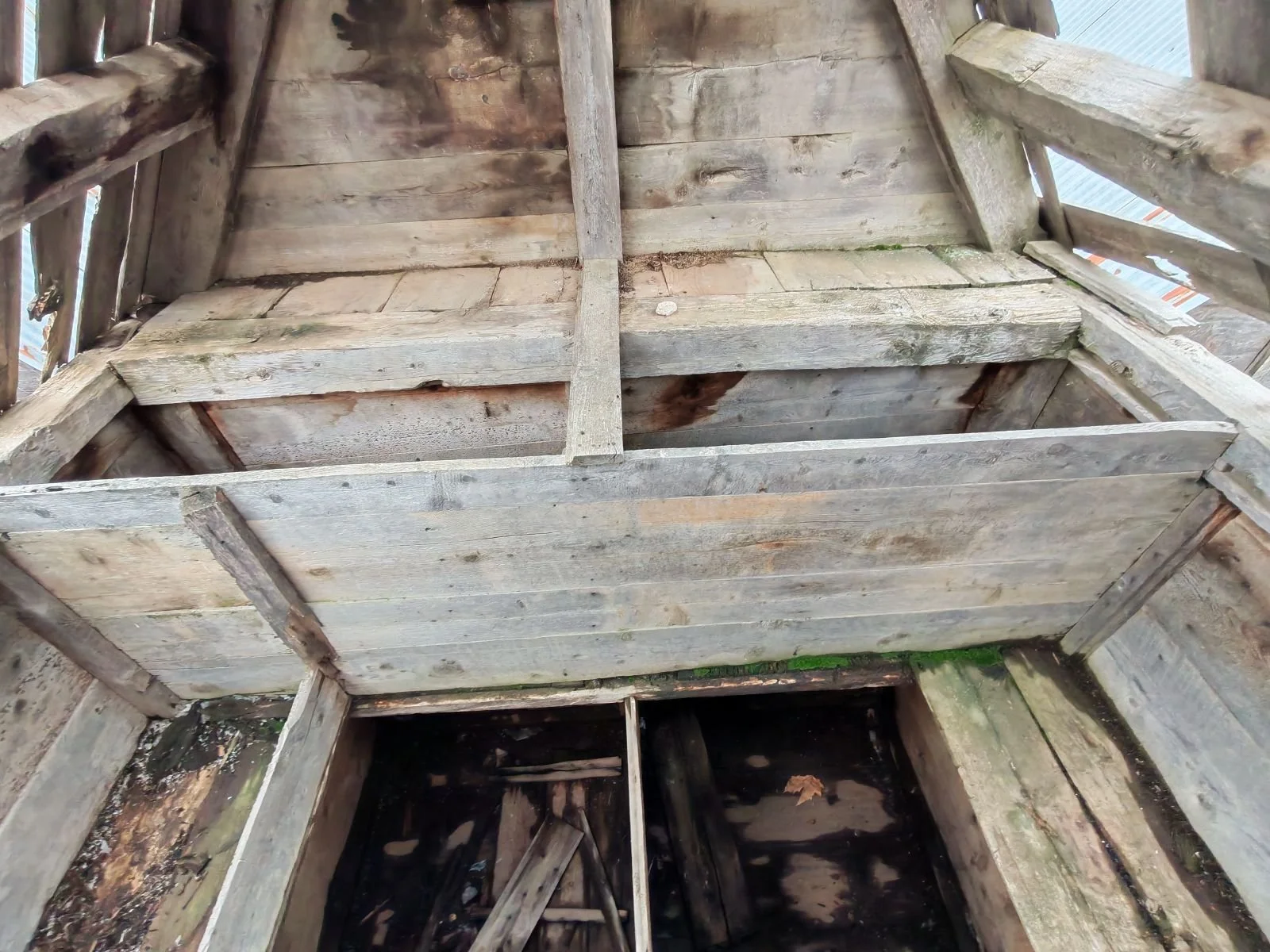 Eski ahşap çatının iç kısmı, ahşap kirişler ve duvarlar visible, bazı yerlerde hasar ve kir bulunuyor.