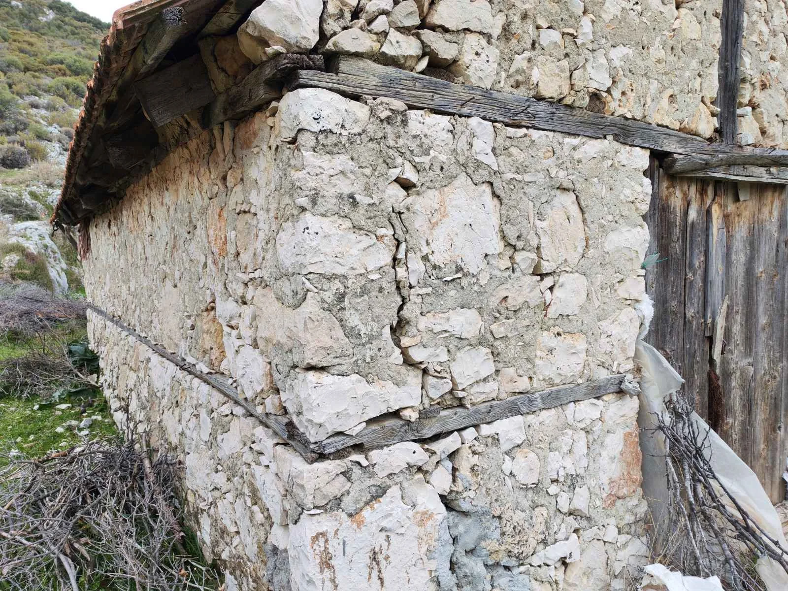 Taş malzeme ve ahşap çerçeveyle inşa edilmiş küçük bir yapı, doğa içinde.