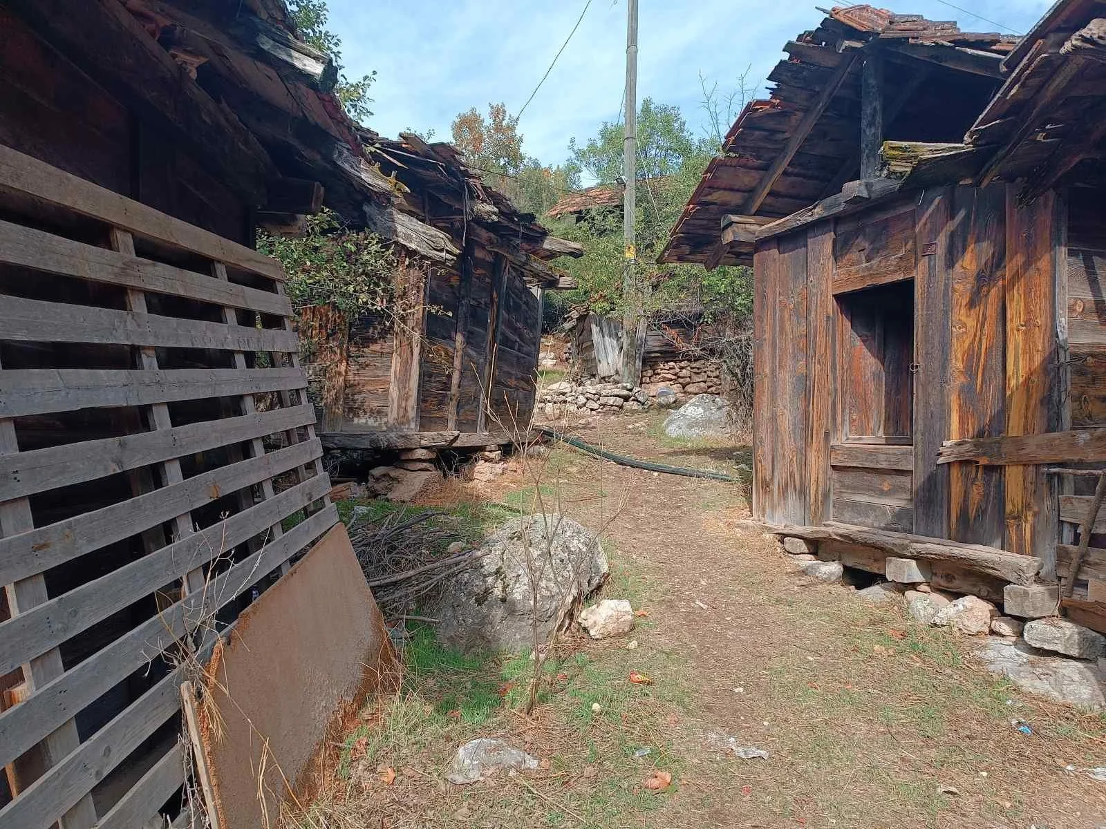 Kırık ahşap evler ve yıkık duvarlar ile eski köy evi yapıları.