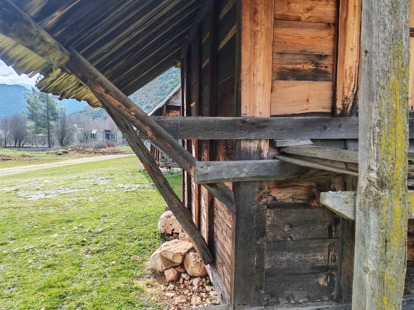 Ahşap eski bir yapıya ait merdiven ve parça duvarlar, doğa ve dağlar ile çevrili kırsal alan.