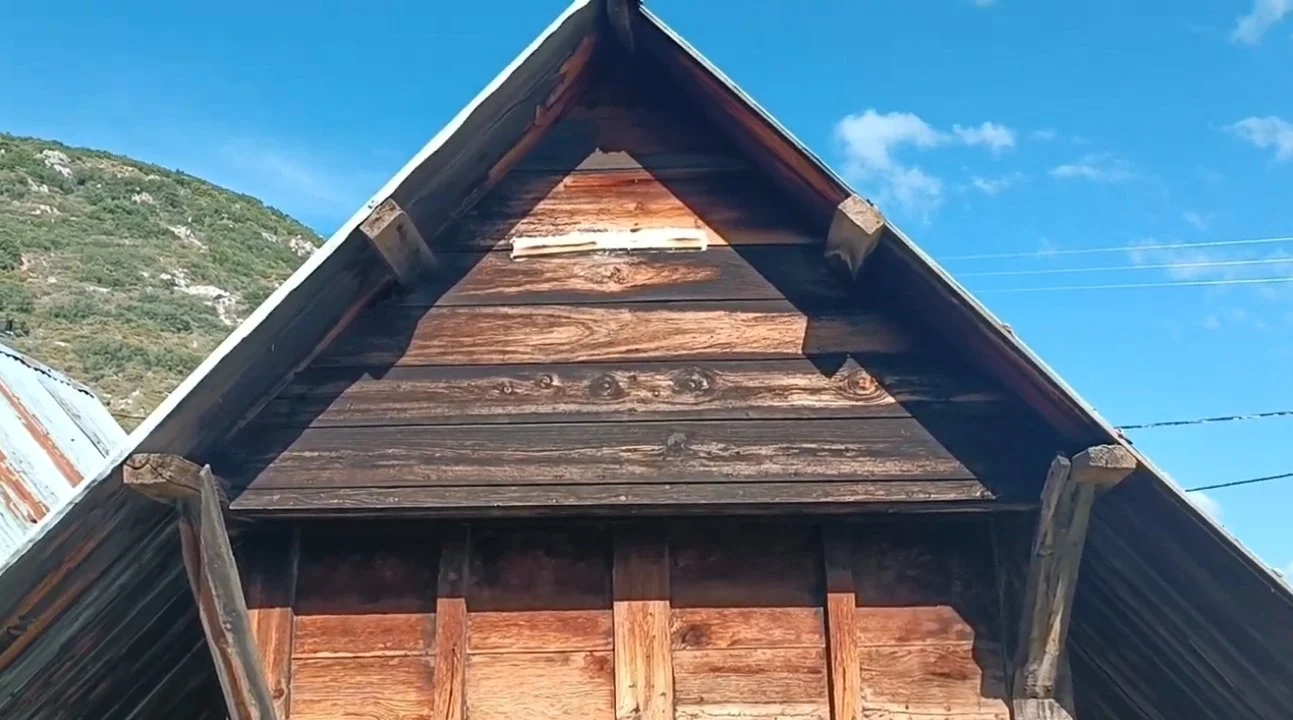 Ağaç ve metal çatıyla kaplı, ahşap bir bina, gökyüzü ve dağlar arka planda