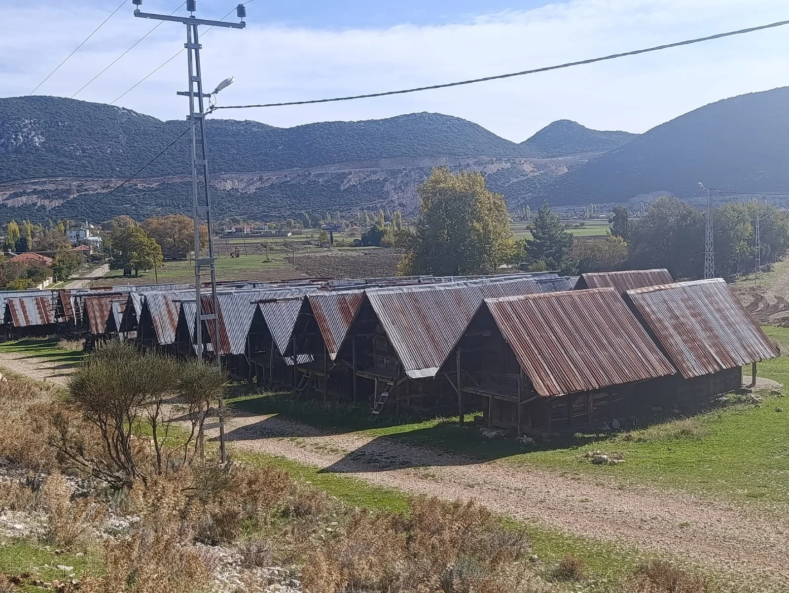 Dağlar önünde sıralanmış, metal çatılı ve ahşap yapılar.
