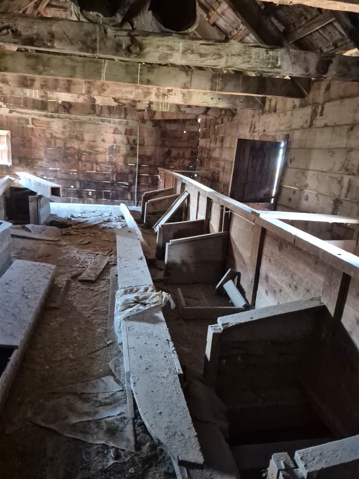 Eski ve kullanılmayan iç mekanı, ahşap duvarlar ve tavan, tozlu ve dağınık, birkaç pencereden az ışık alıyor.