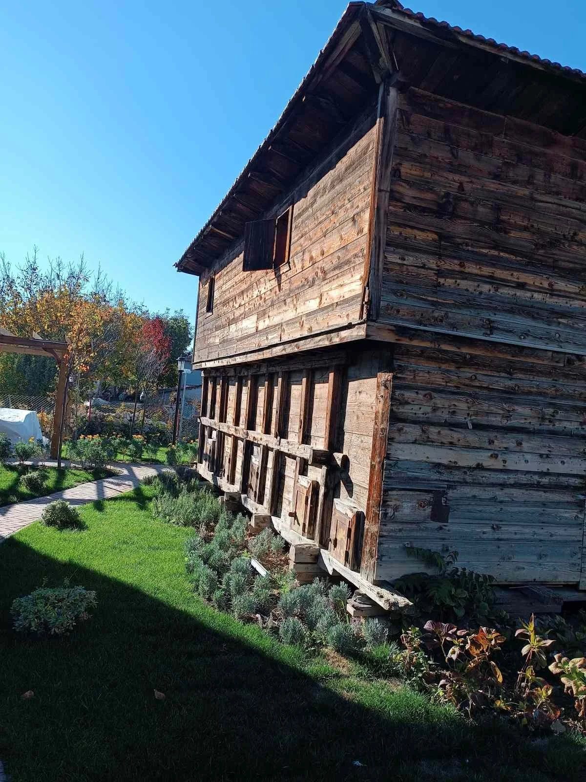 Ahşap bir ev, bahçe ve bazı ağaçlar gökyüzü açık mavi renkte