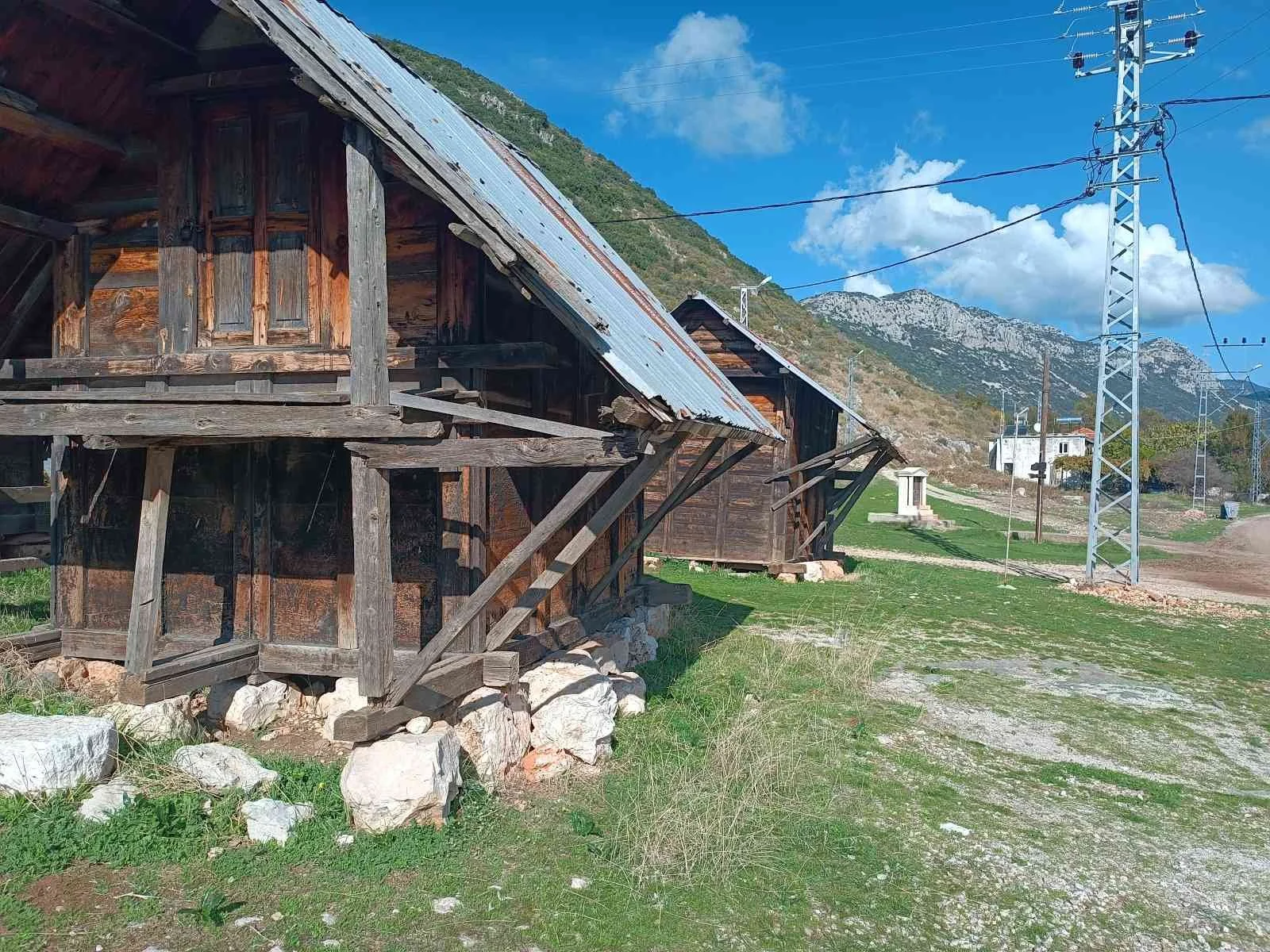 Eski ahşap yapılar ve elektrik direkleriyle dağlık bir alanda yer alan kırsal alan.