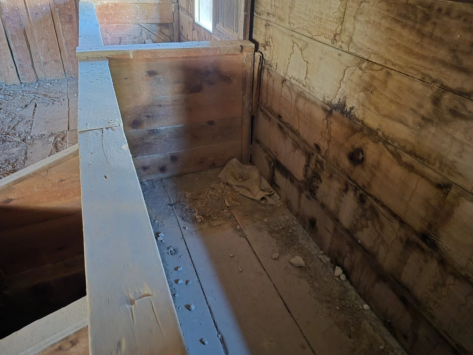 İçeride, ahşap duvarlar ve zemin görülen inşaat alanı. Zemin toprak ve taş parçaları ile dolu, duvarlar eski ve çatlamış ahşaptan yapılmış.