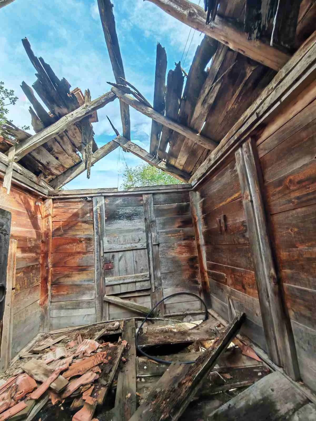 Halı kullanılamaz halde, çatısı tamamen yıkılmış veya hasar görmüş eski ahşap ev.