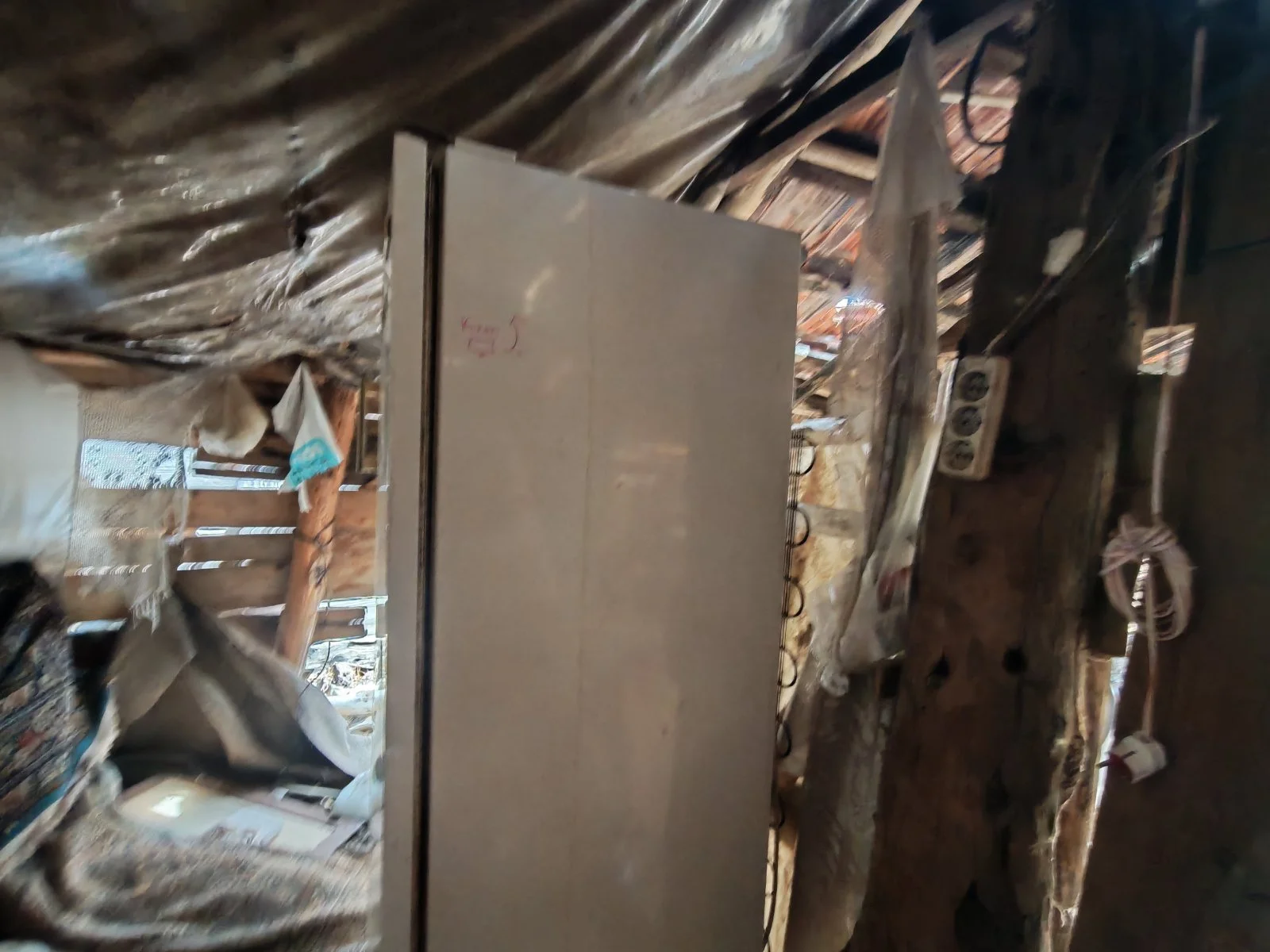 Eski ve bakımsız ahşap yapıda oda. Odanın köşesinde eski elektrik prizi ve birkaç elektrikli cihaz bulunuyor. Odanın duvarları ve tavanı ahşap ve bakımsız görünüyor.