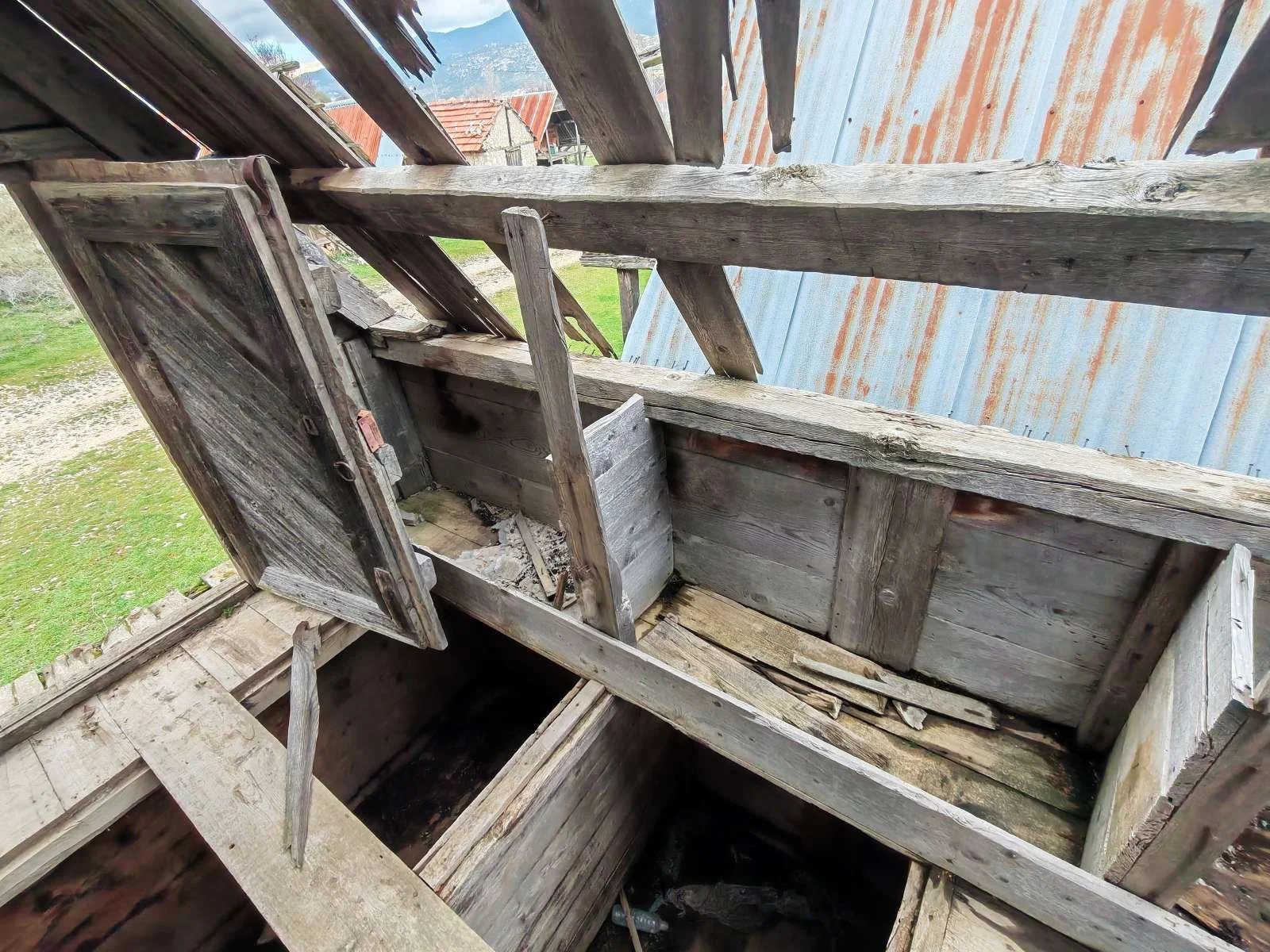 Eskimiş ve hasar görmüş, ahşap malzemelerden yapılmış eski bir bina veya kulübe. Çökme ve deformasyonlar mevcut.