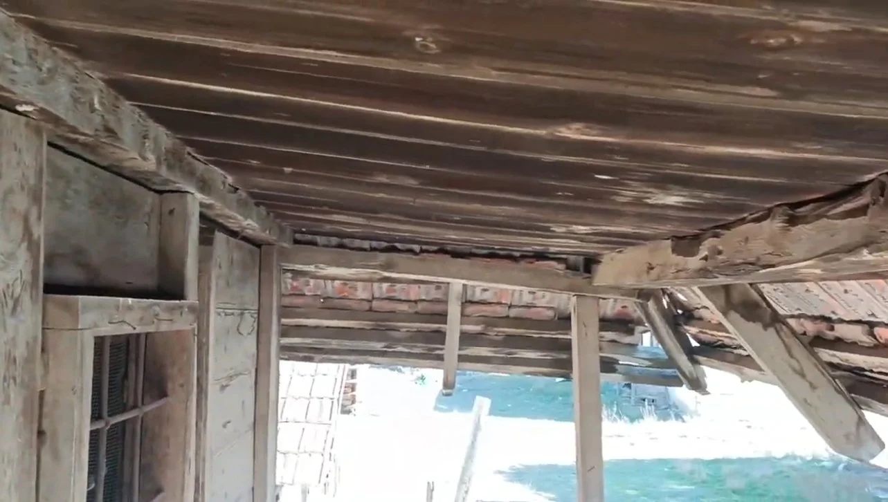 Ahşap çatısında hasar olan eski bir yapı. Çatının bazı kısımları kırık ve deforme olmuş.