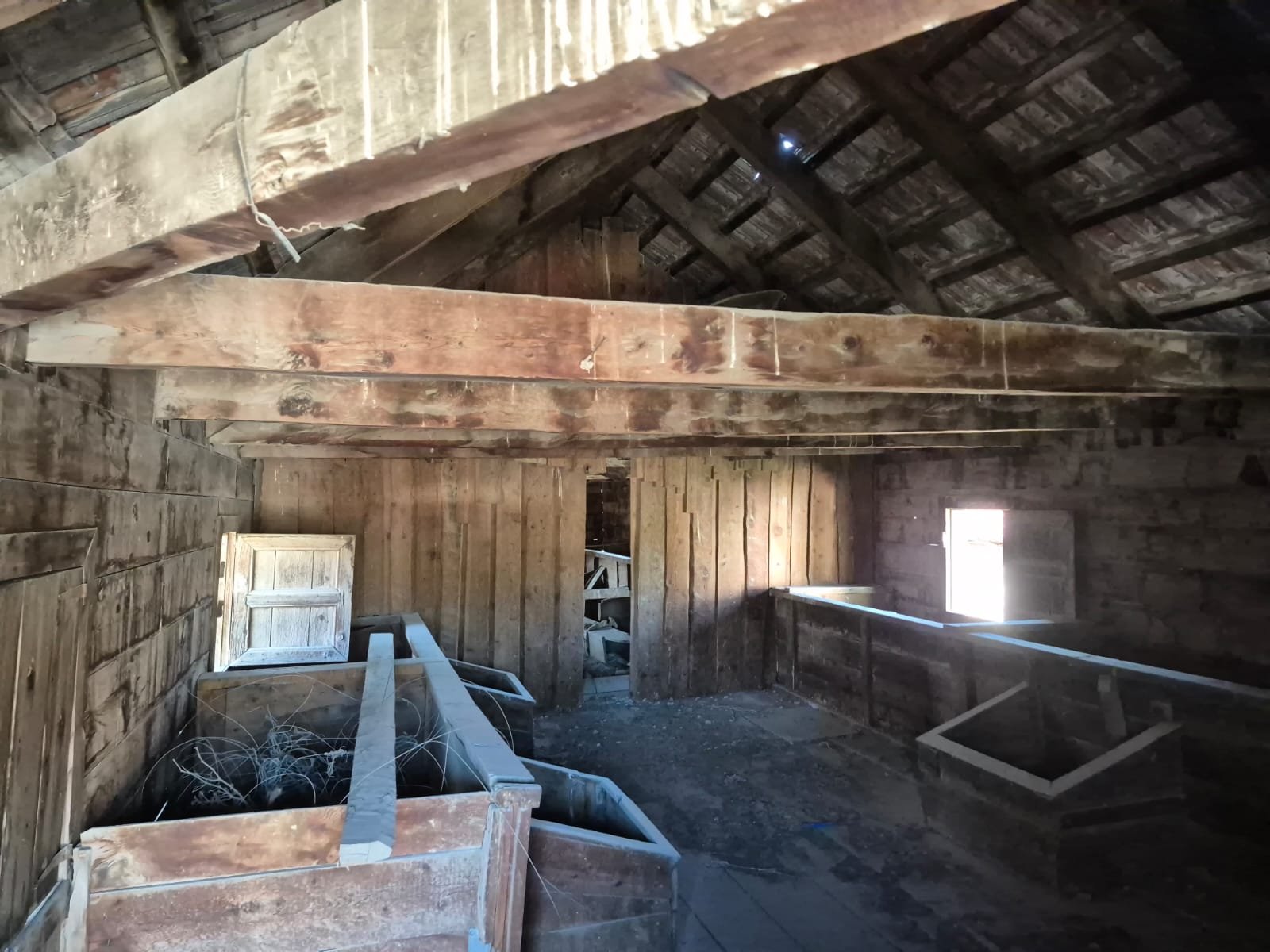 Eski, ahşap bir çatı ve duvarlara sahip ahır veya tavan alanı, bazı eski ahşap kutular ve çeşitli nesneler var, küçük bir pencere ile aydınlatılmış.