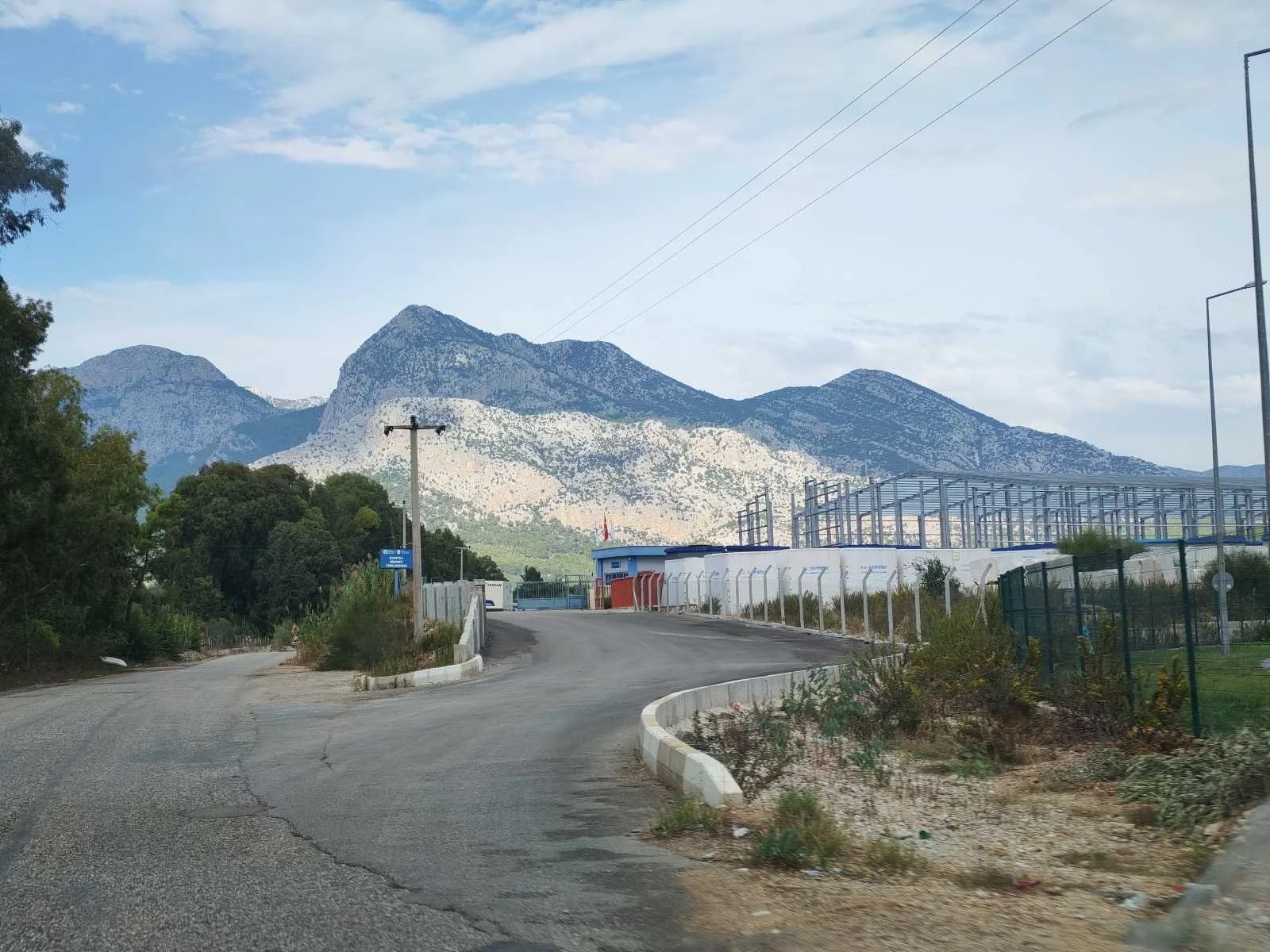 Dağlar ve yol, yol kenarında some binalar ve elektrik direkleri var, gökyüzü açık ve hafif bulutlu.